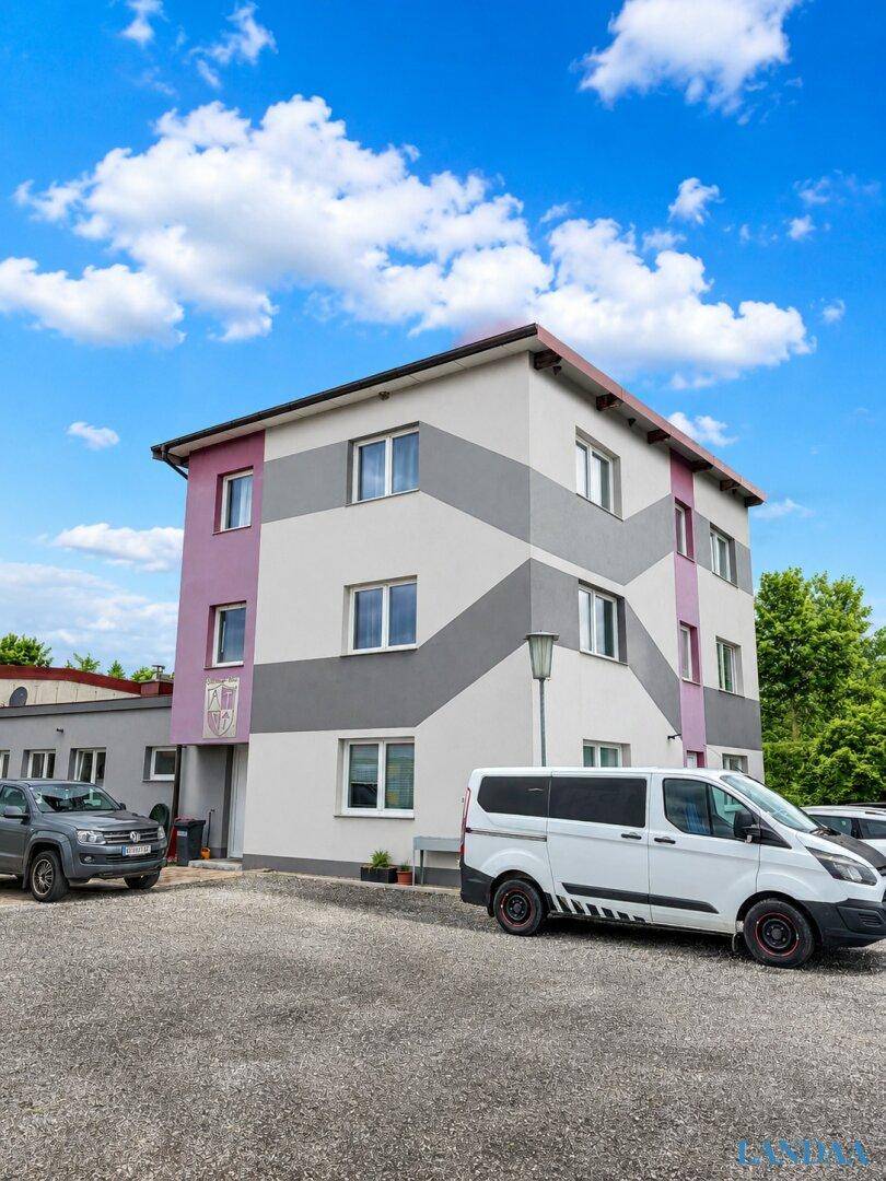 Modernes mehrstöckiges Gebäude mit auffälliger grau-violetter Fassadengestaltung, umgeben von einem Parkplatz.