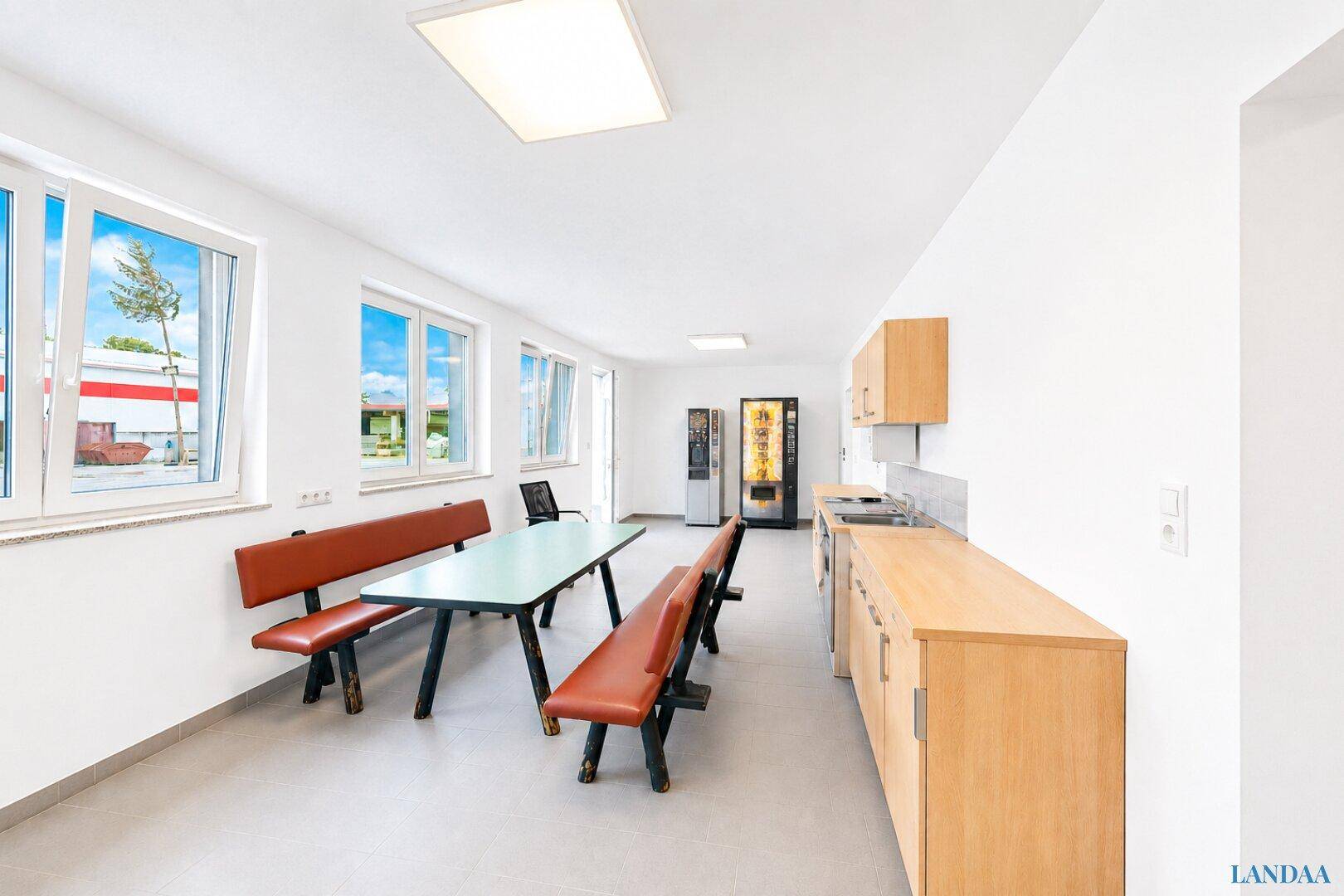 Gemütlicher Pausenraum mit langer Tafel, Bänken, kleiner Küchenzeile und Verkaufsautomaten für Mitarbeiter.