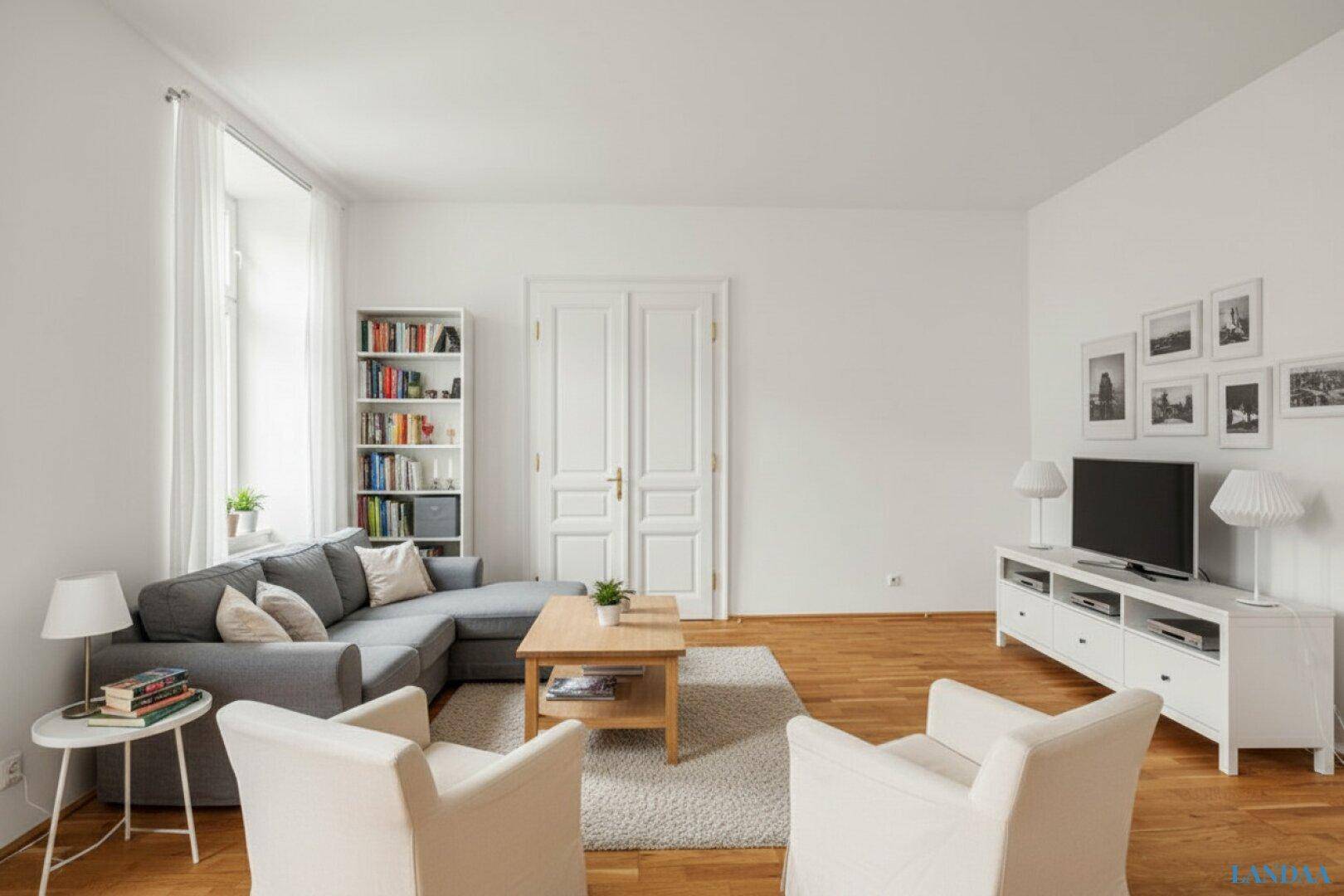 Helles Wohnzimmer mit Parkettboden, einem bequemen Ecksofa und einem Bücherregal.