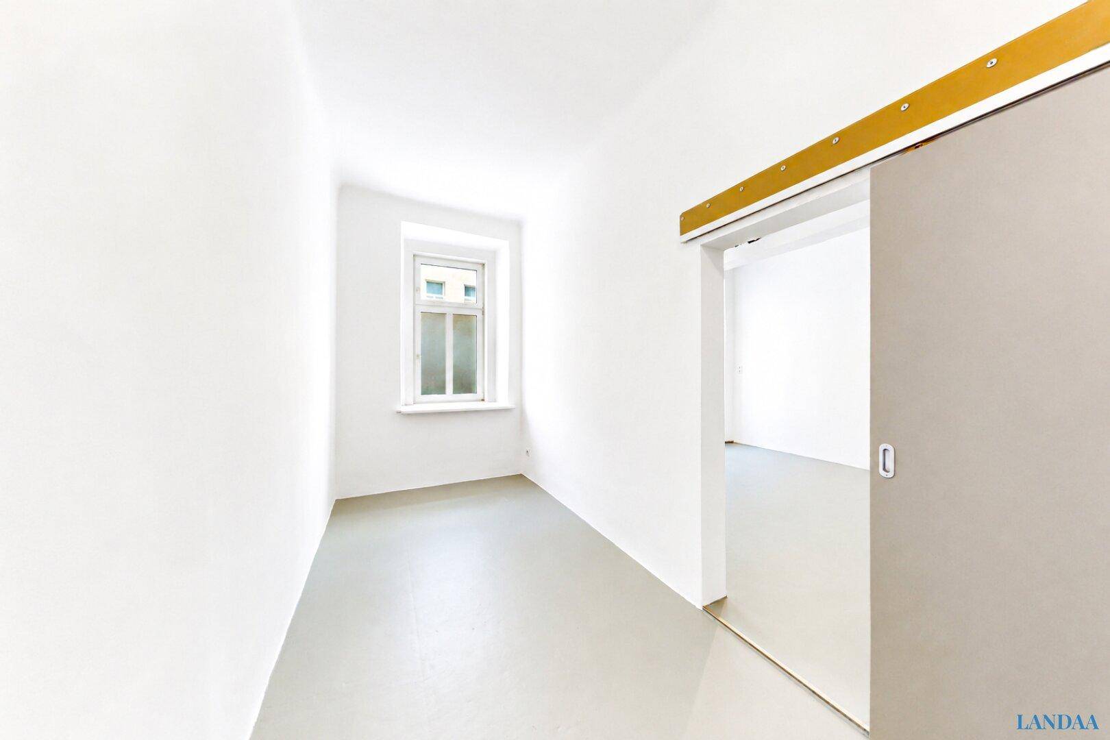 Schmaler, heller Raum mit hellem Boden und einem Fenster, ideal als kleines Büro oder Gästezimmer.
