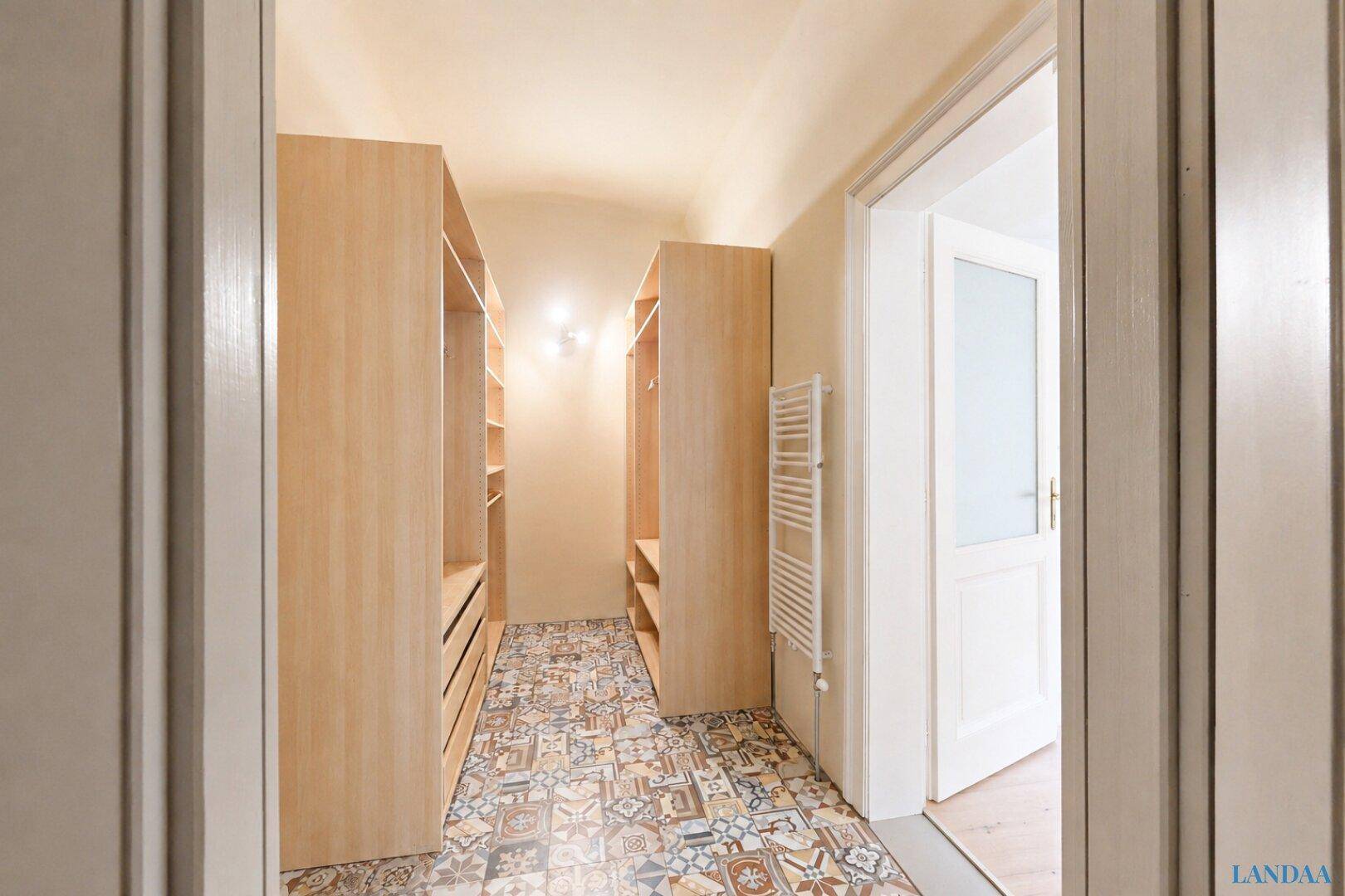 Begehbarer Kleiderschrank mit gemusterten Fliesen und offenen Holzregalen für Kleidung.