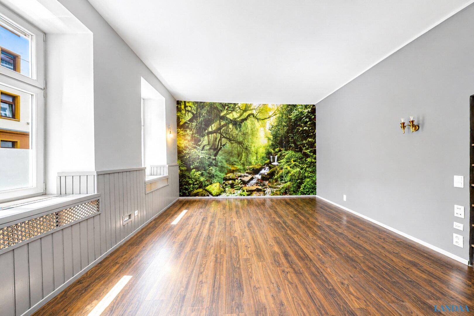 Heller Raum mit Holzboden, grauen Wänden und einer großen Wandtapete mit Waldmotiv.