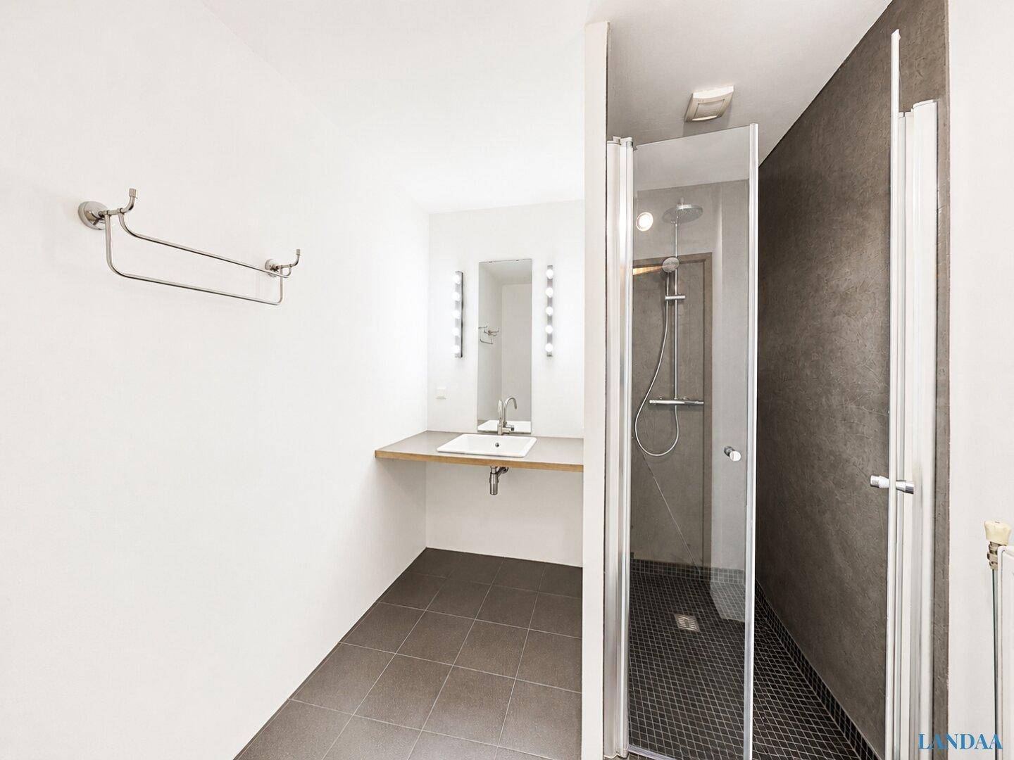 Modernes Badezimmer mit Waschtisch, großem Spiegel und einer begehbaren Dusche mit dunklen Fliesen.