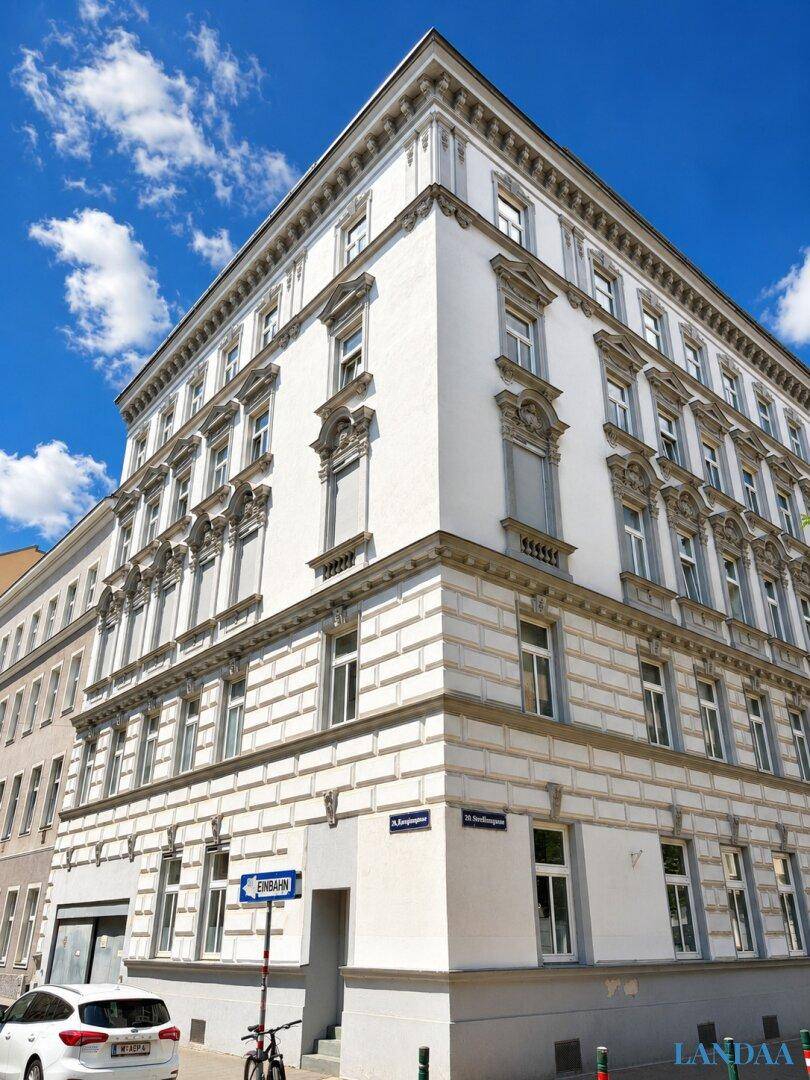 Eckgebäude mit klassischer Architektur und weißer Fassade an einem sonnigen Tag.