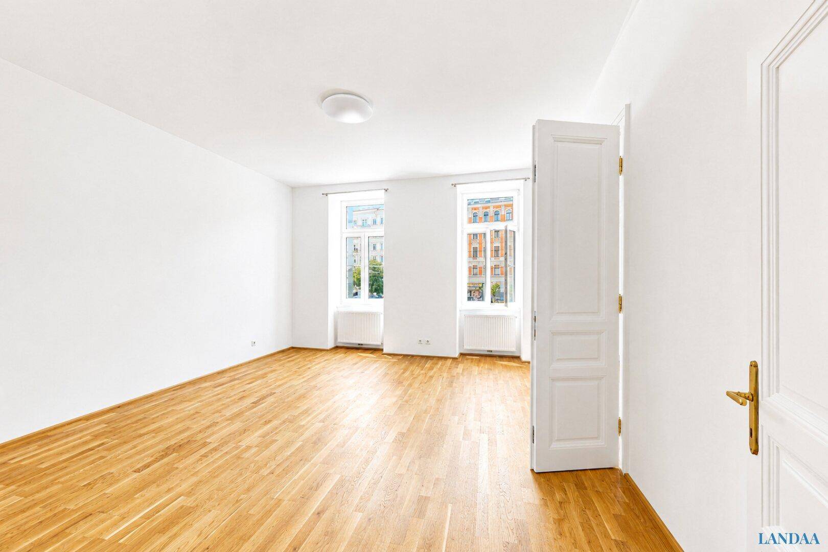 Geräumiges, helles Zimmer mit Parkettboden und zwei großen Fenstern, ideal als Wohn- oder Schlafzimmer.