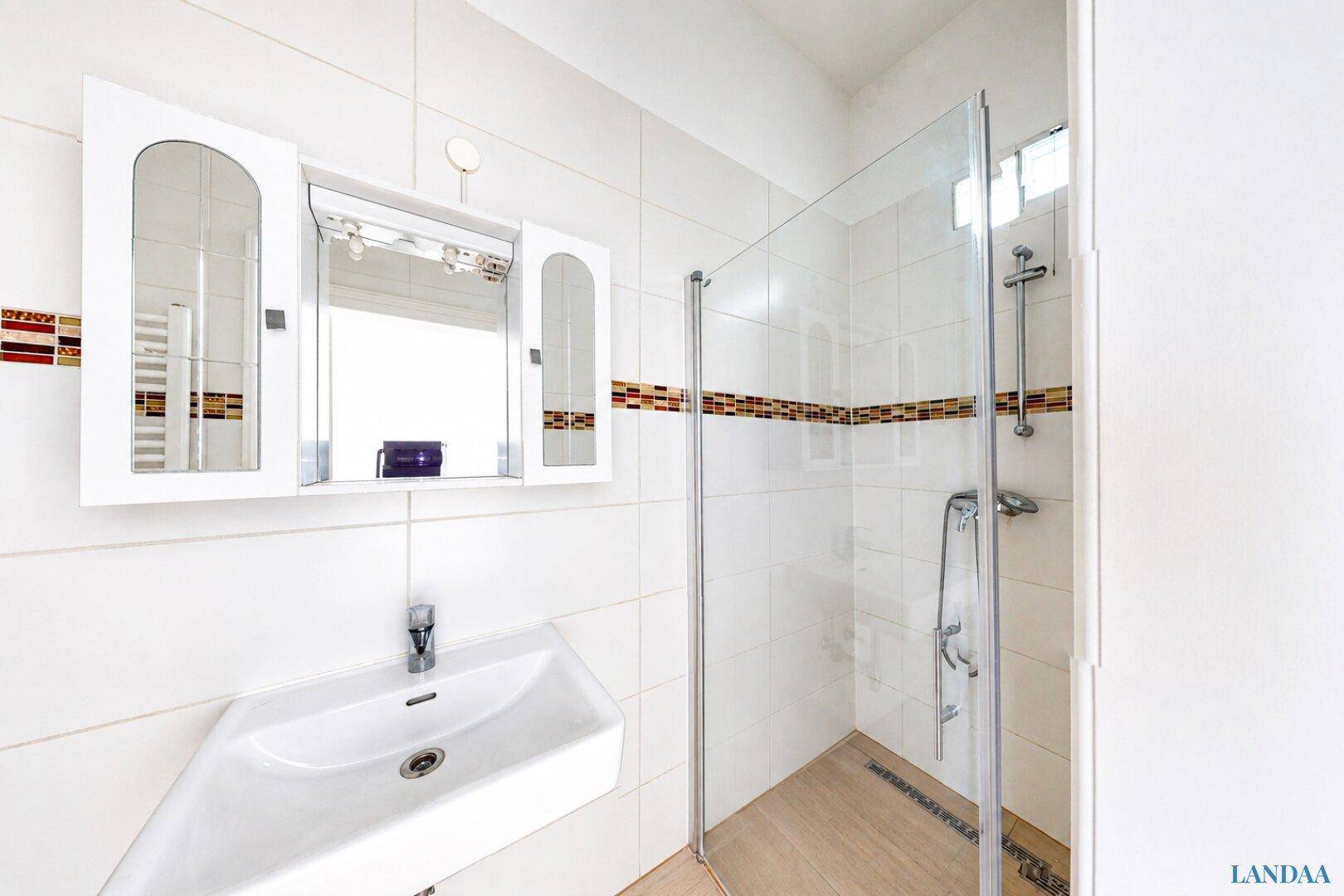 Modernes Badezimmer mit Duschkabine, Waschbecken und Spiegelschrank, hell gefliest.