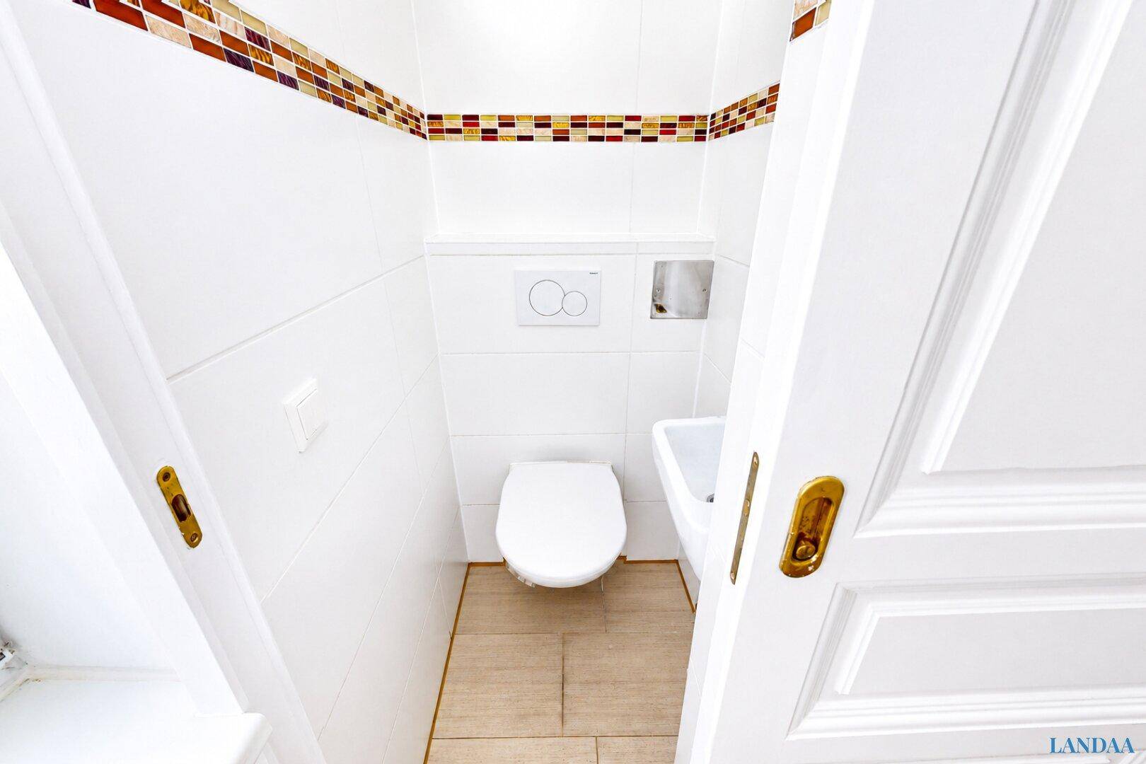 Kleines Gäste-WC mit Wand-WC, Waschbecken und dekorativen Fliesenbordüren.