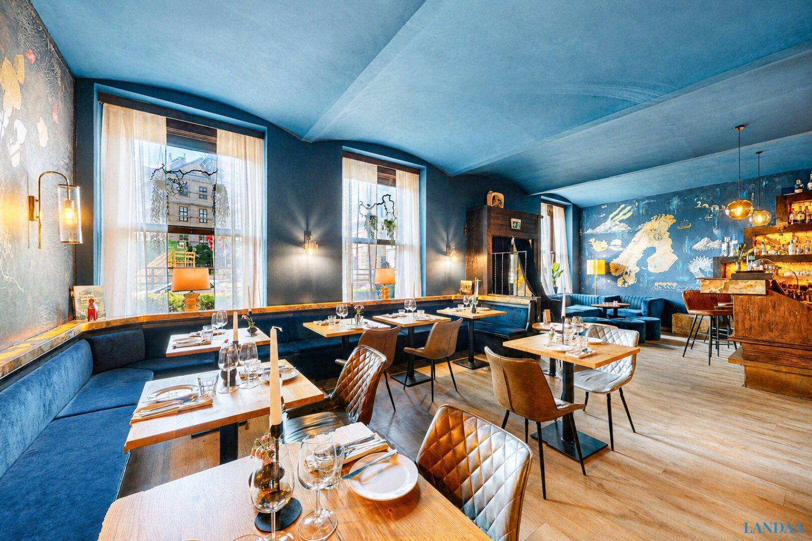 Stilvoller Restaurantbereich mit blauen Sitzbänken, Holztischen und großen Fenstern für viel Tageslicht.