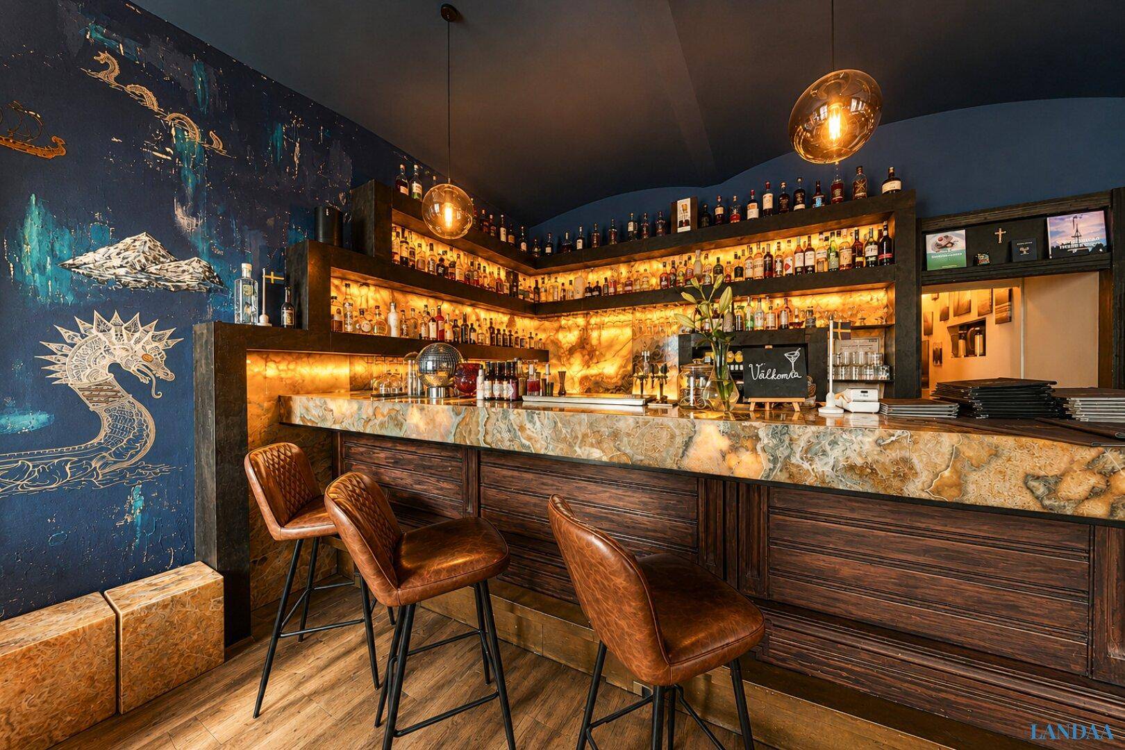 Detailansicht der Bar mit beleuchteter Theke, Ledersesseln und einer kunstvollen Wandgestaltung.
