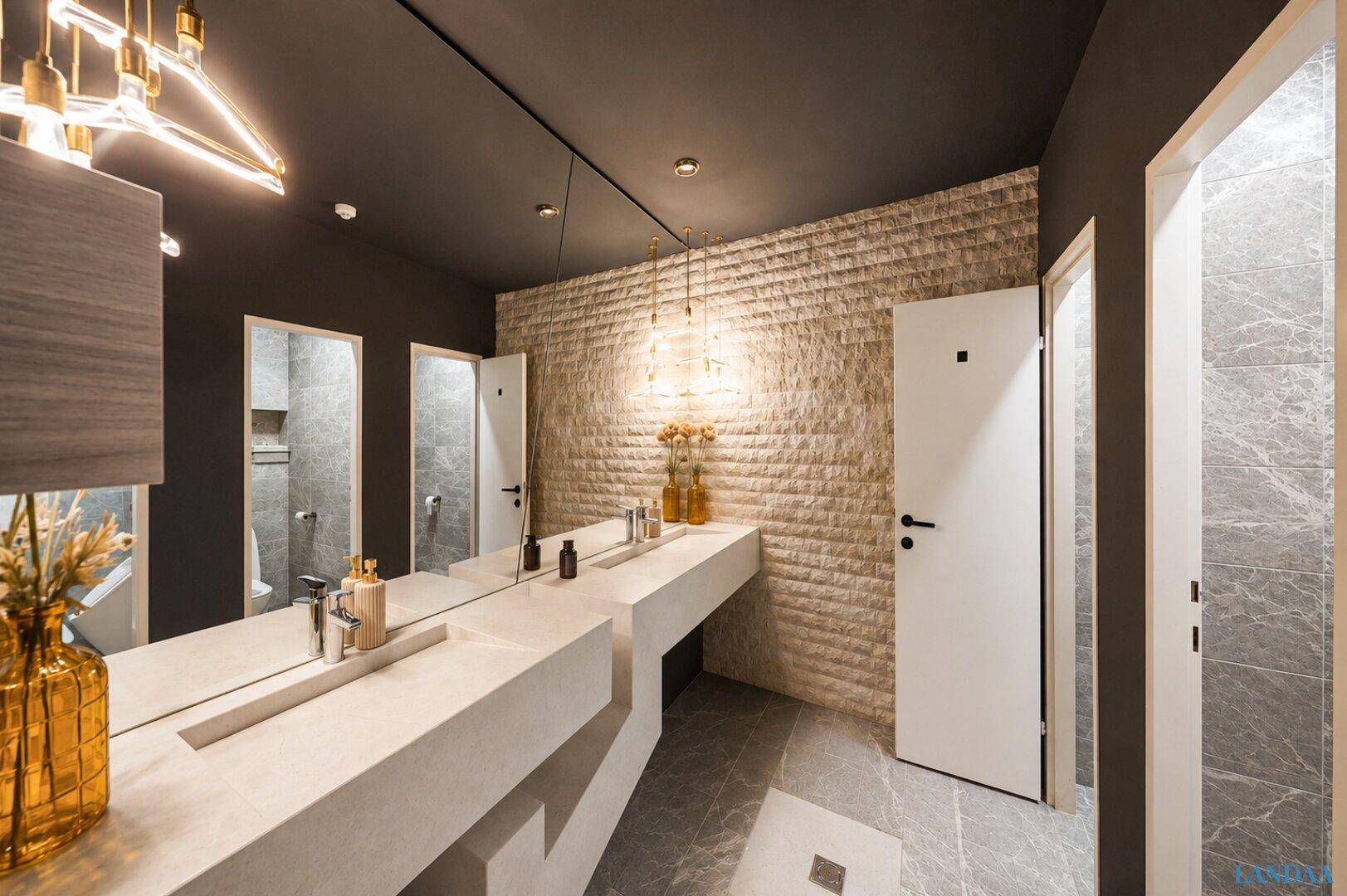 Moderner Waschraum mit zwei Waschbecken, großem Spiegel und strukturierten Wandfliesen in Beige.