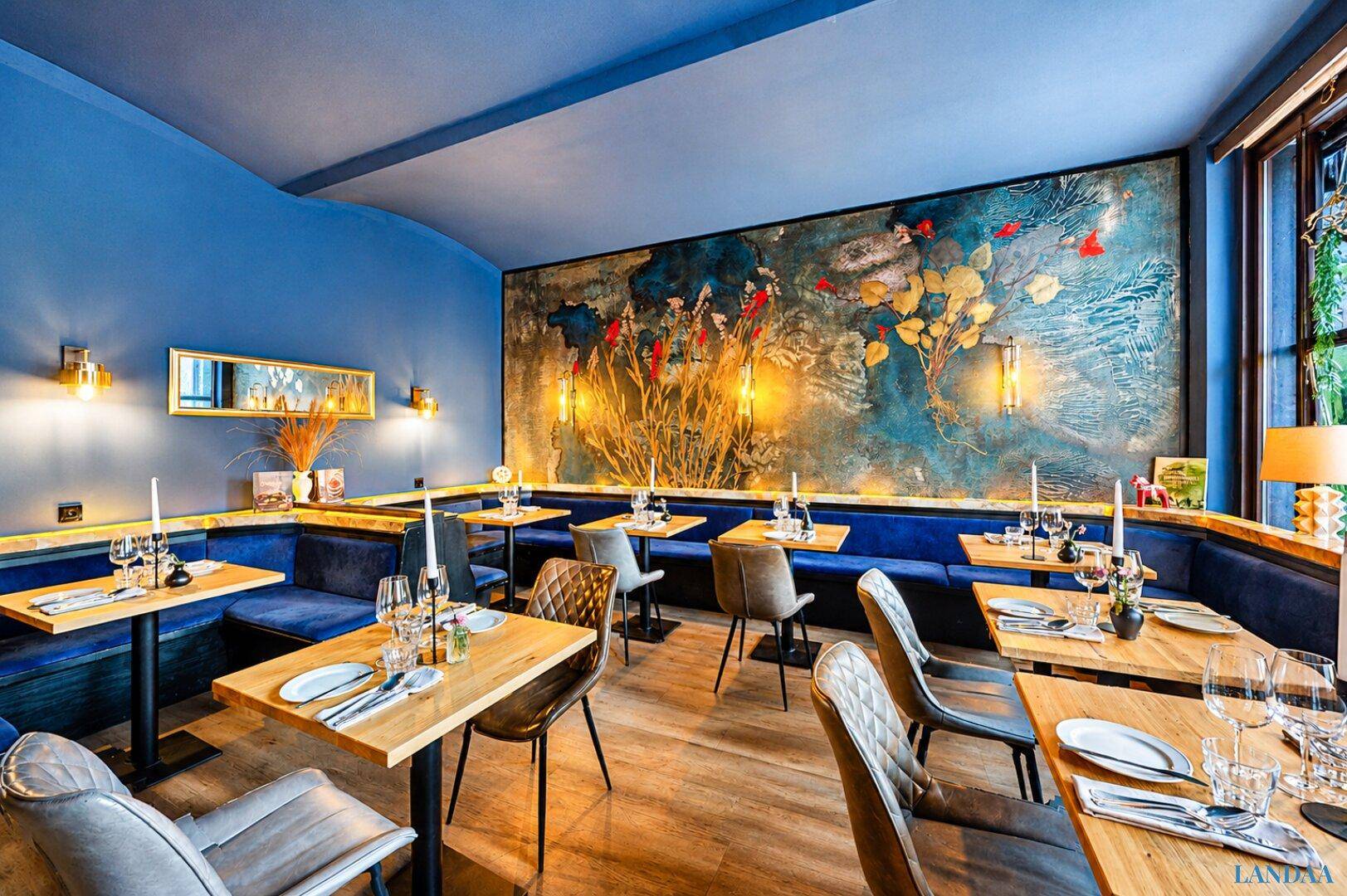 Restaurantbereich mit blauen Sitzbänken, Holztischen und einer auffälligen Wandmalerei als Blickfang.