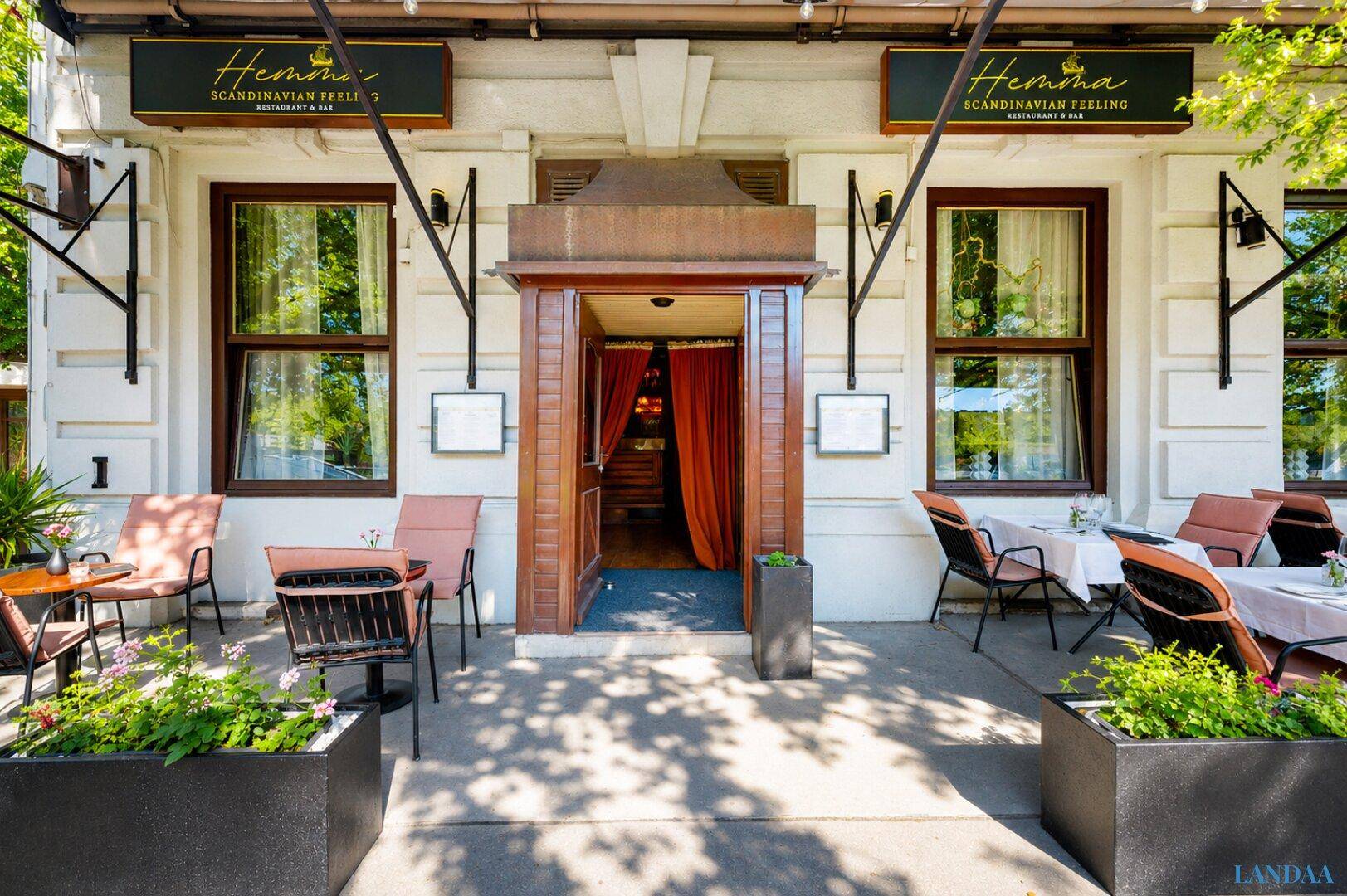 Eingangsbereich des Restaurants mit Außenterrasse, geschmückt mit Pflanzen und bereit für Gäste.