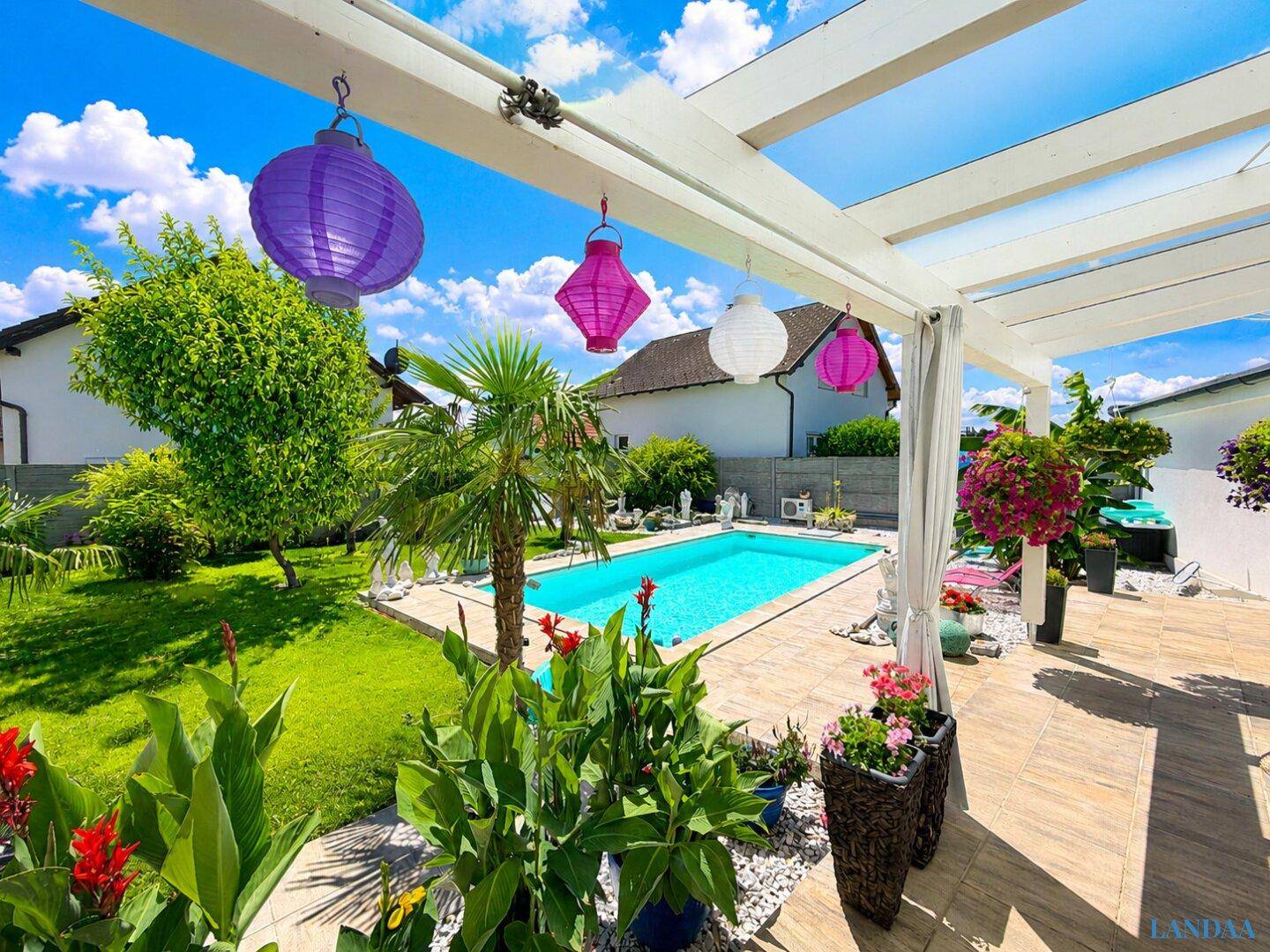 Gemütliche Terrasse mit bunten Laternen, Pflanzen und Blick auf den Poolbereich.