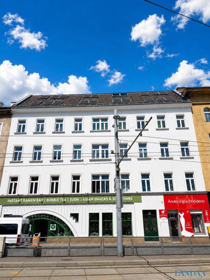 Gebäudefassade mit mehreren Stockwerken und Geschäften im Erdgeschoss unter blauem Himmel.