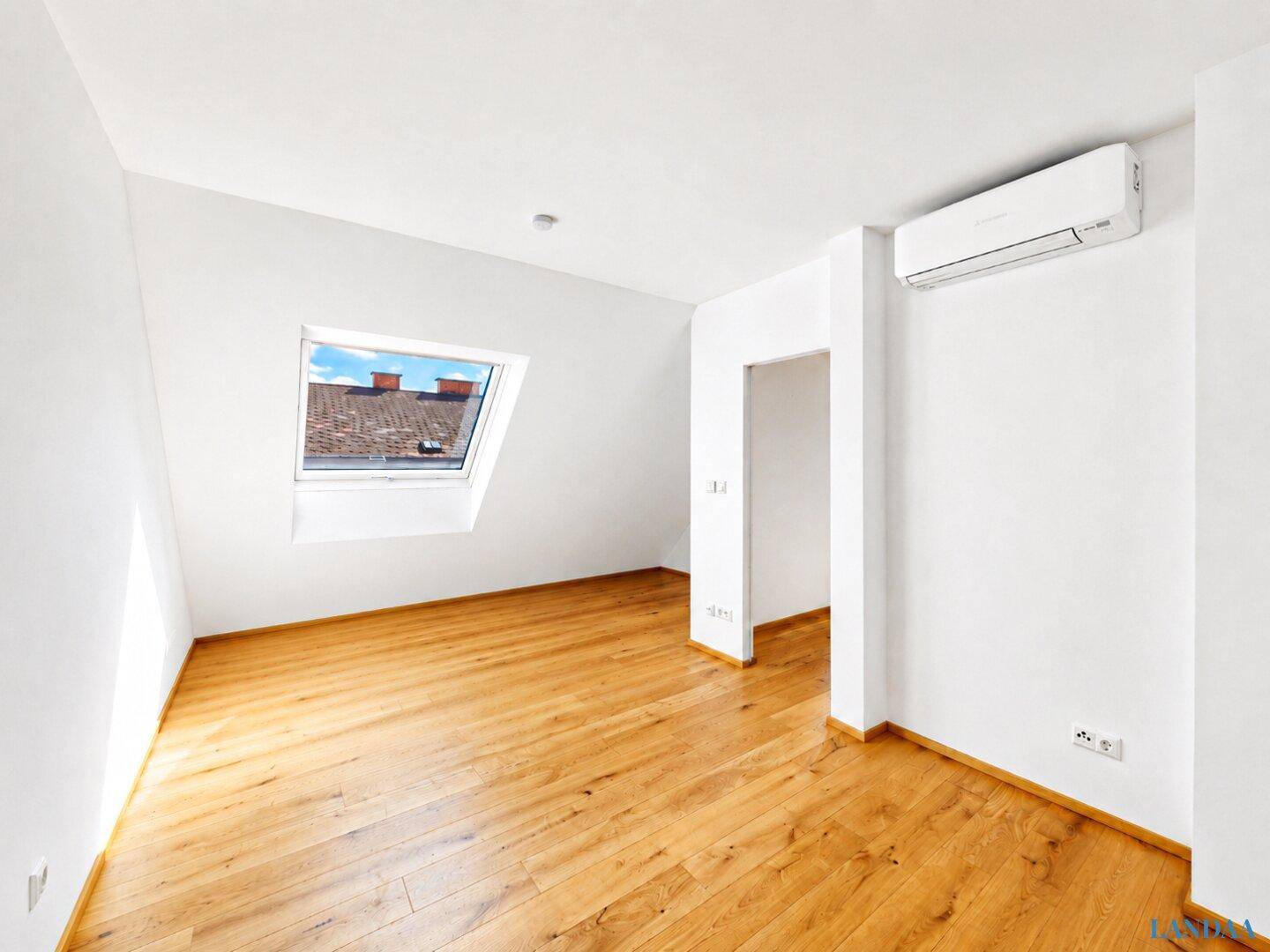 Helles Schlafzimmer im Dachgeschoss mit Holzboden und Dachfenster.