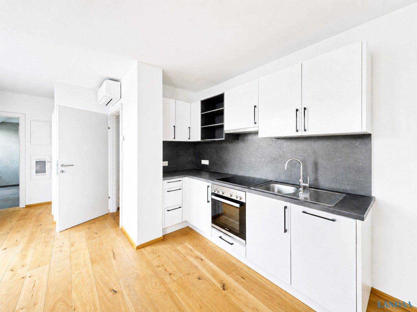 Moderne Küchenzeile mit weißen Schränken, dunkler Arbeitsplatte und Holzboden.