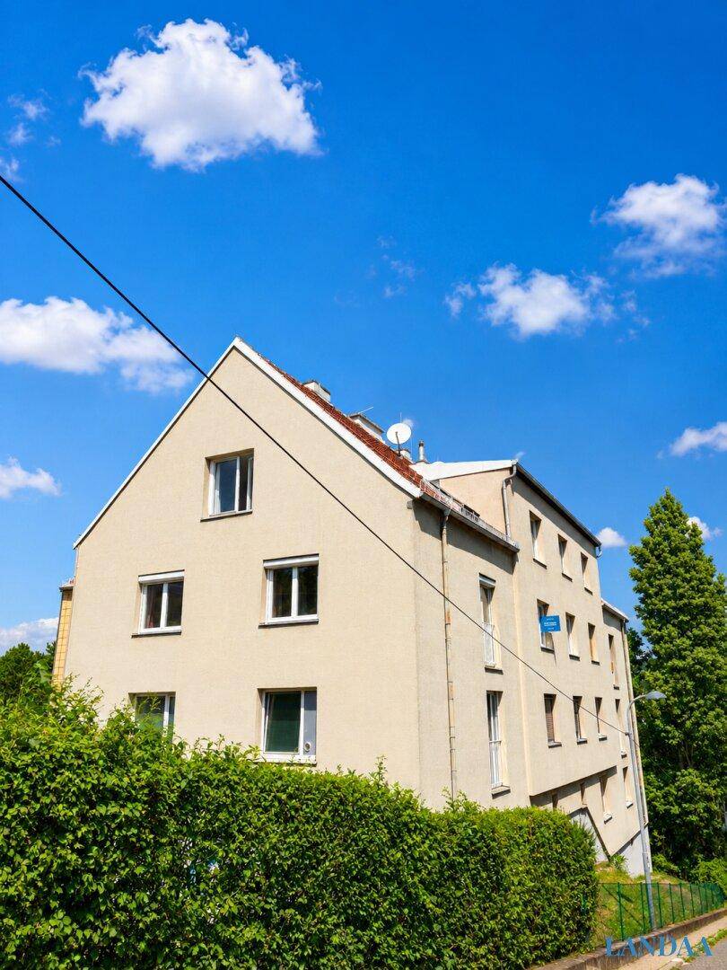 Mehrfamilienhaus mit heller Fassade und Satteldach unter blauem Himmel mit Wolken.