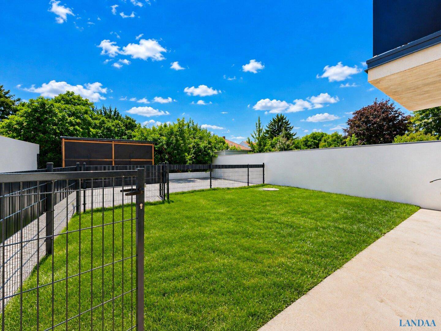 Gepflegter Rasenbereich im Garten mit Zaun und viel Grün unter blauem Himmel.