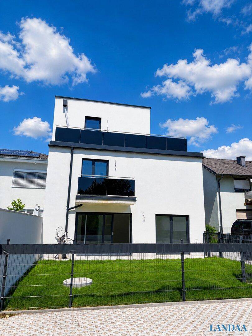 Moderne weiße Fassade eines Neubaus mit Balkonen und kleinem Vorgarten.