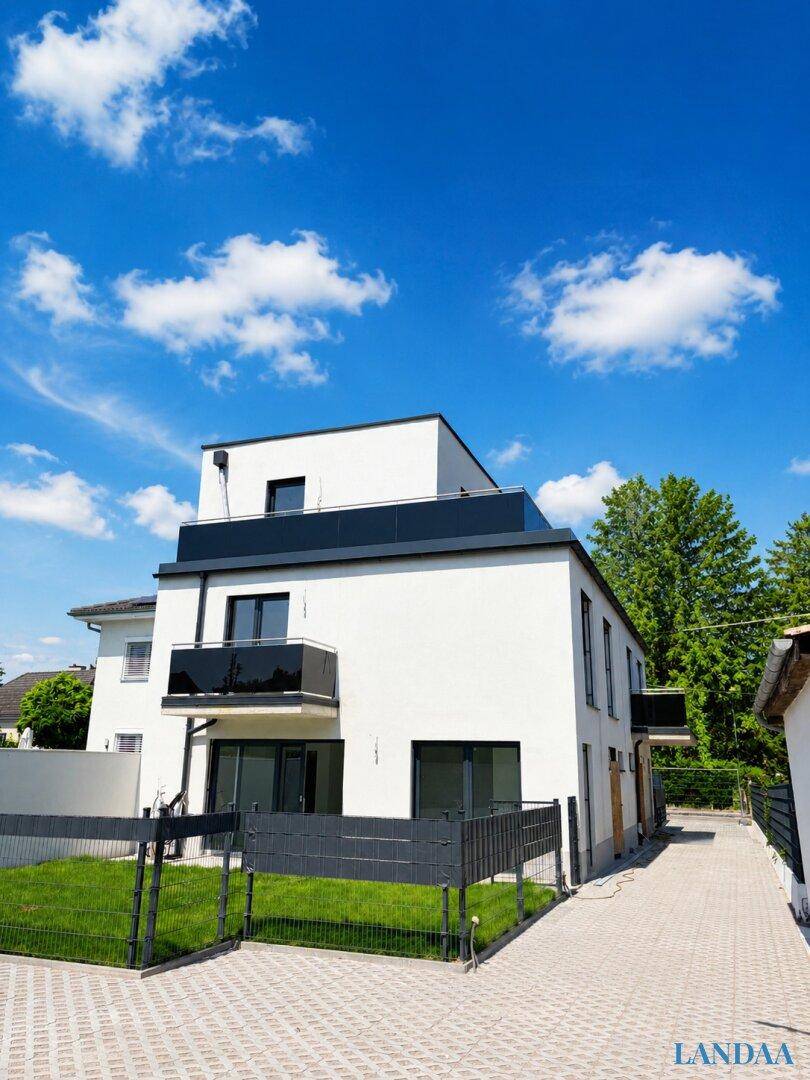 Moderner Neubau mit weißer Fassade, Balkonen und gepflasterter Zufahrt.