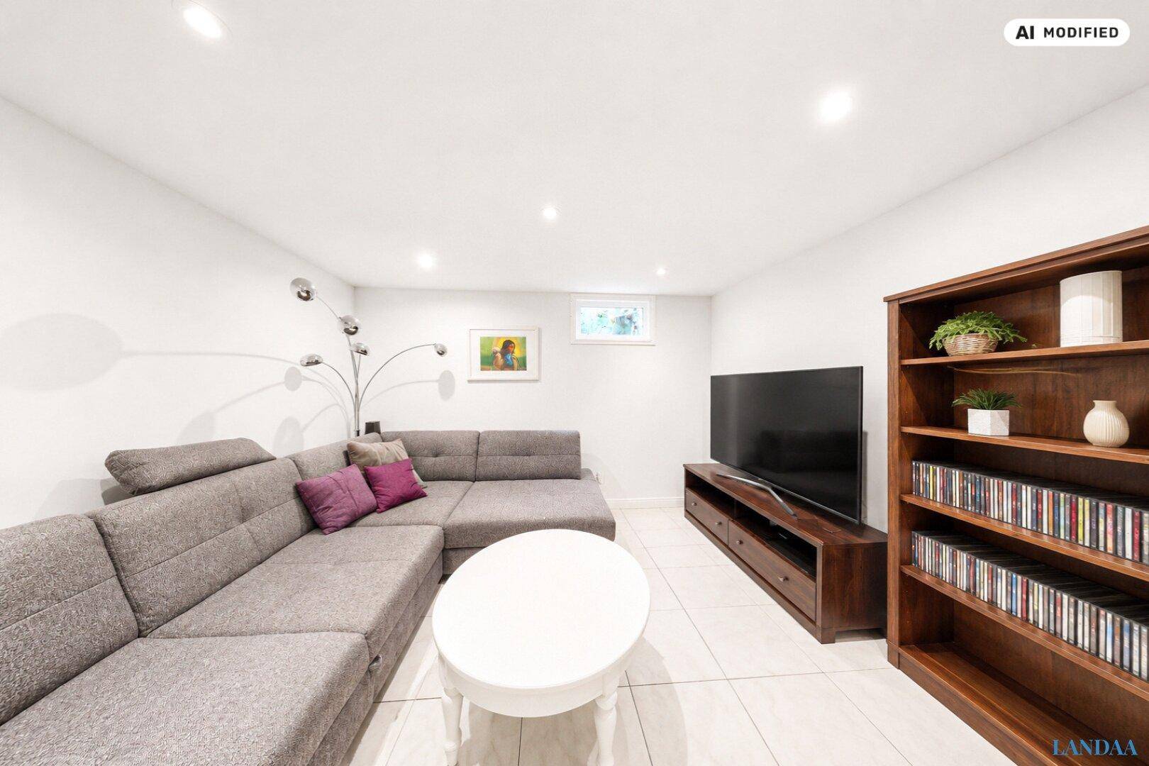 Gemütlicher Wohnbereich im Untergeschoss mit großem Sofa, Fernseher und Bücherregal.