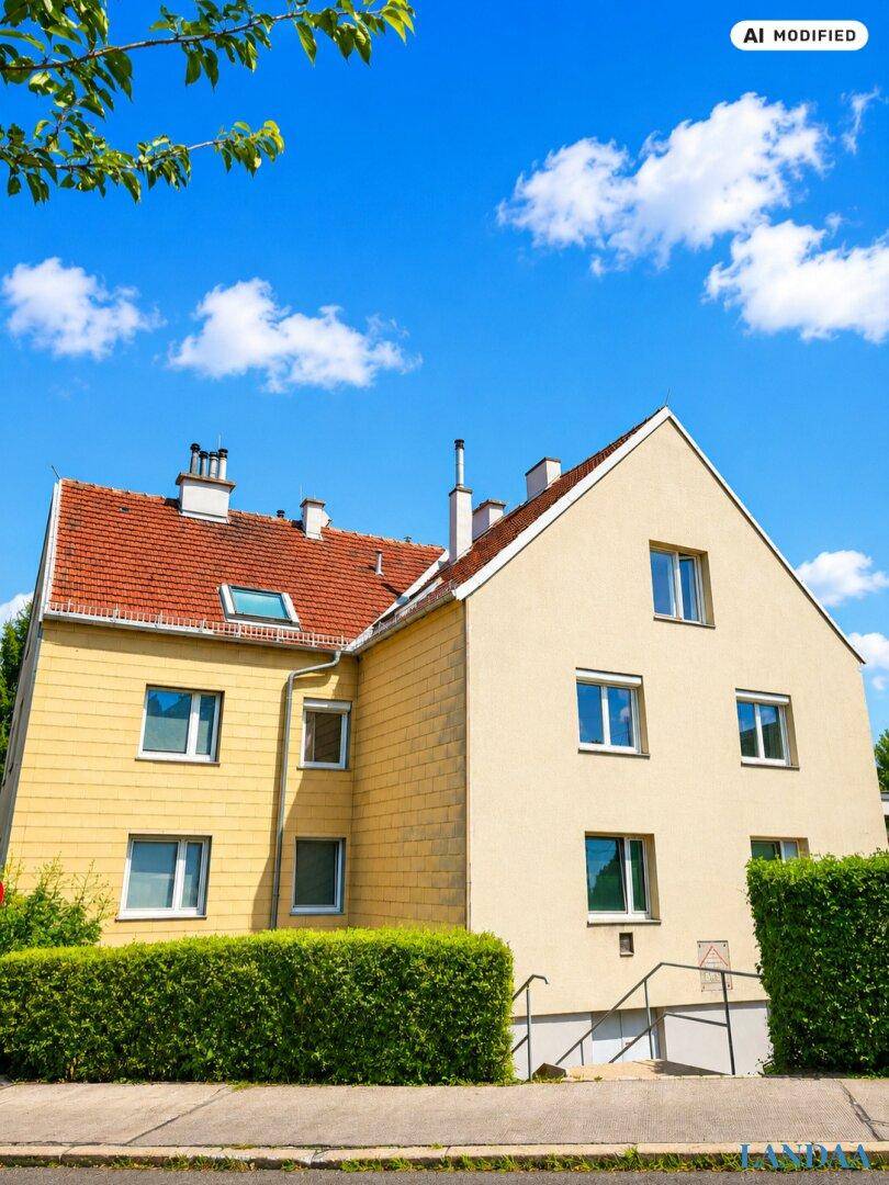 Rückansicht eines Wohnhauses mit gelber Fassade, rotem Ziegeldach und grüner Hecke.