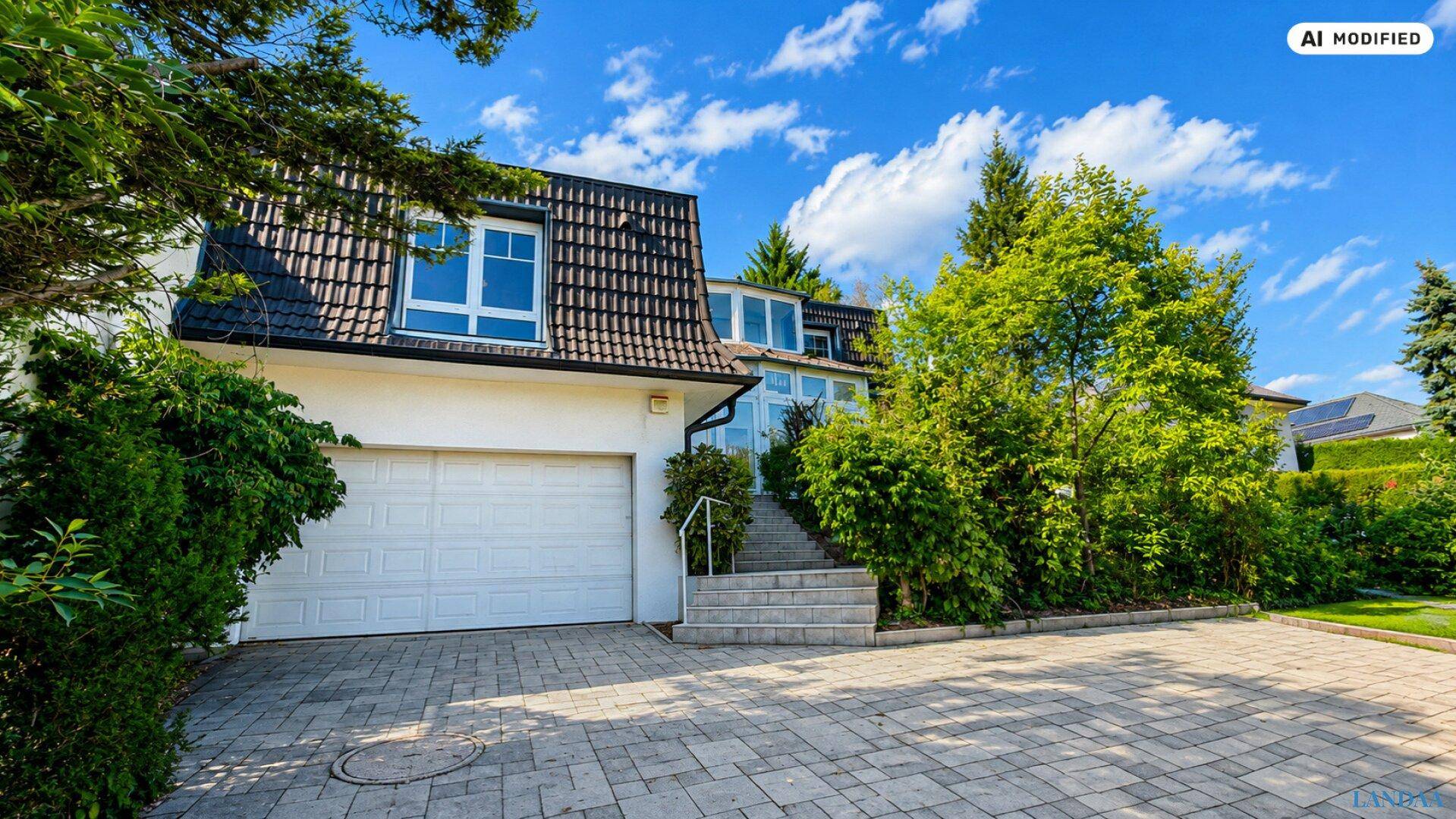 Vorderansicht des Hauses mit integrierter Garage, gepflasterter Auffahrt und Mansarddach.