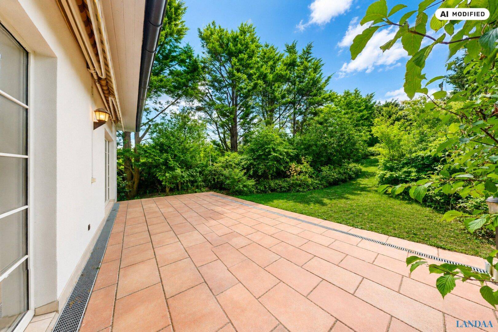 Geräumige, gepflasterte Terrasse mit Blick auf den weitläufigen, grünen Gartenbereich des Anwesens.