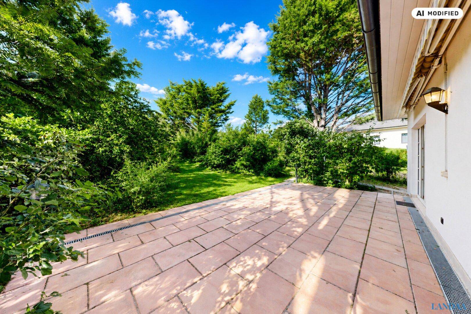 Weitläufige, gepflasterte Terrasse mit angrenzendem Rasenbereich und üppiger Bepflanzung.