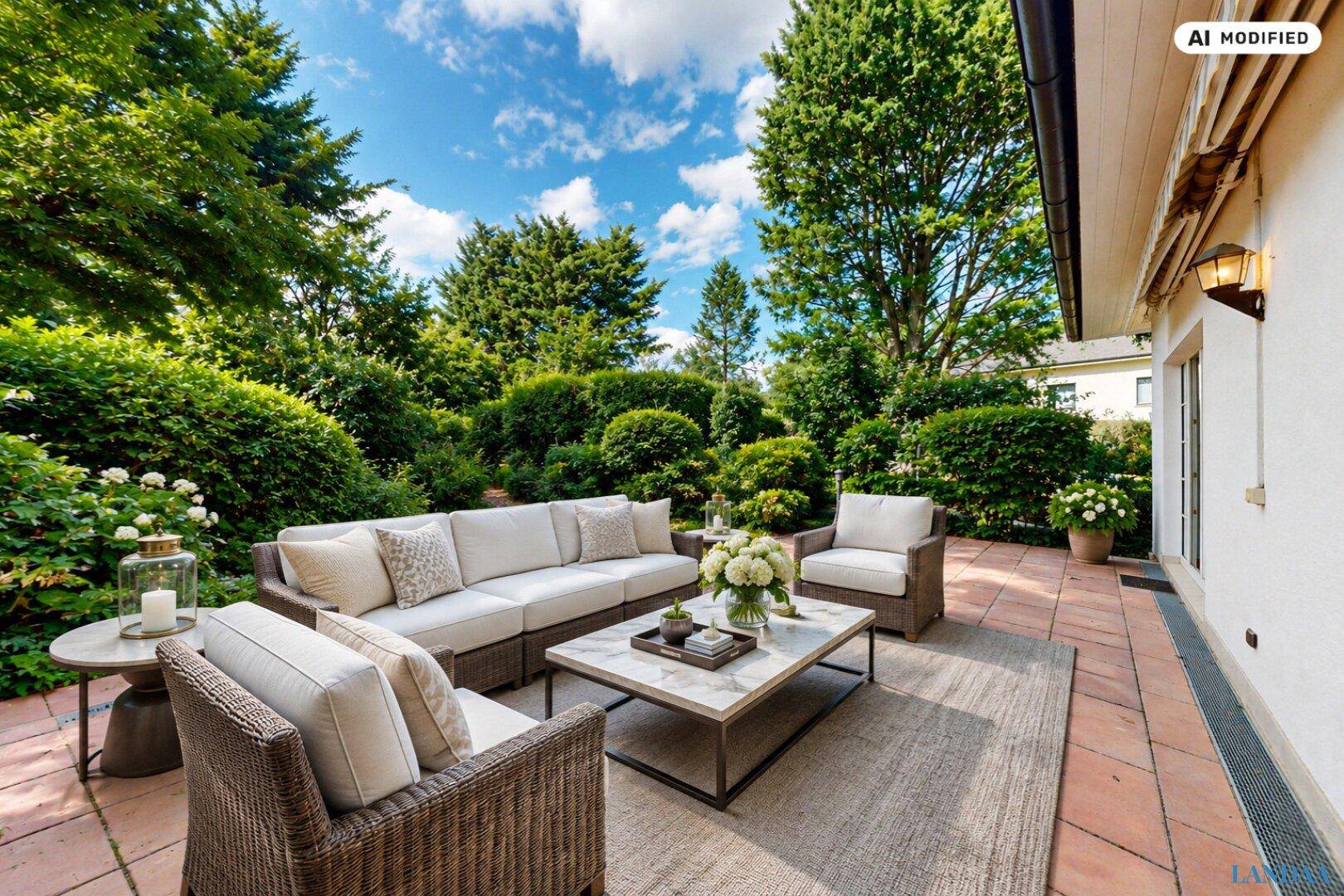 Gemütliche Terrasse mit bequemen Outdoor-Möbeln, umgeben von gepflegten Hecken und Bäumen.