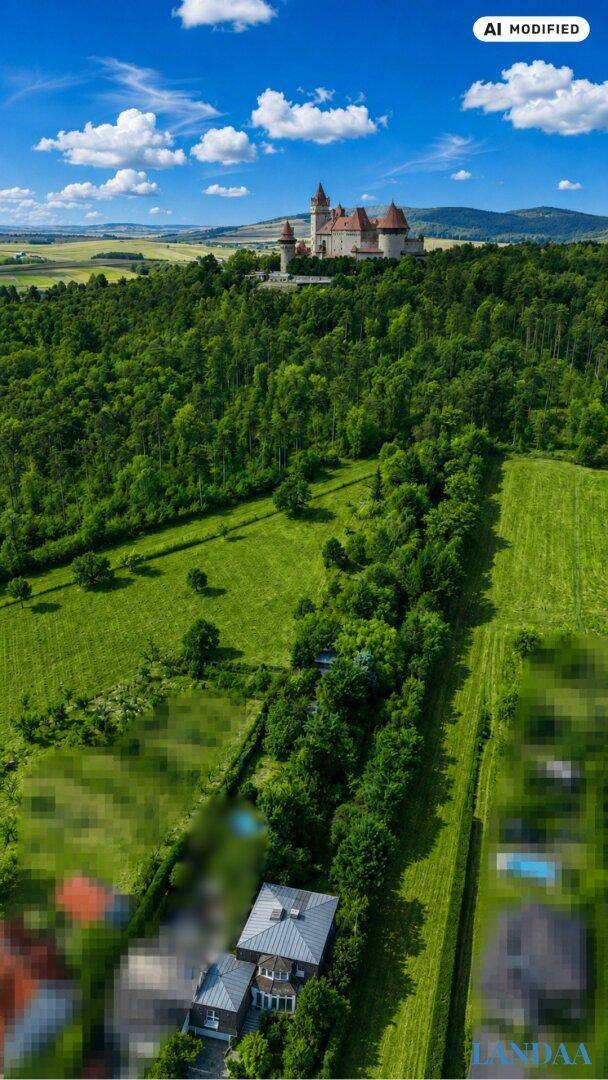 Weitläufige Luftaufnahme der Landschaft mit einem Schloss auf einem Hügel und dem Anwesen im Vordergrund.
