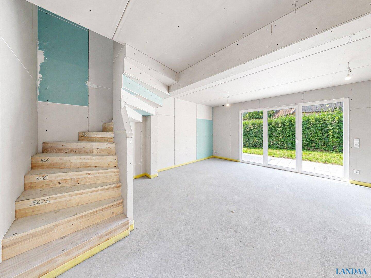 Unfertiger Wohnbereich mit Treppe, großen Fenstern und Zugang zum Garten.
