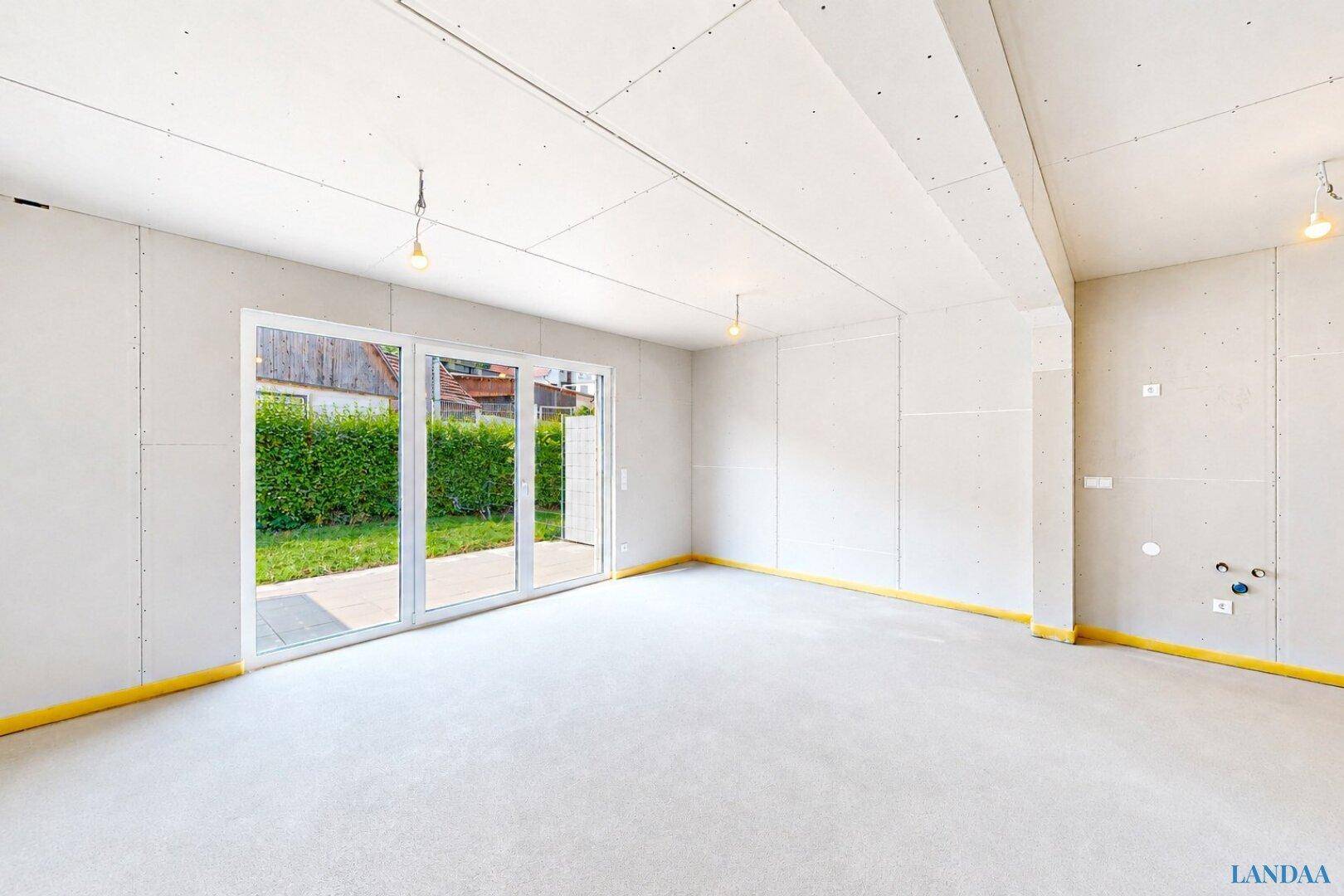 Geräumiger Rohbau-Wohnraum mit großen Glasfronten und direktem Zugang zum zukünftigen Garten.