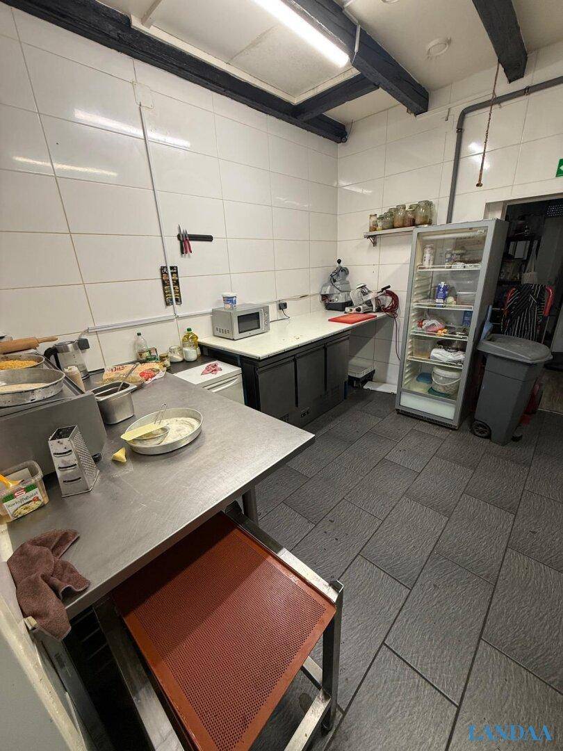 Geräumige Gewerbeküche mit Edelstahlarbeitsflächen, Kühlschrank und weißen Wandfliesen für die Hygiene.