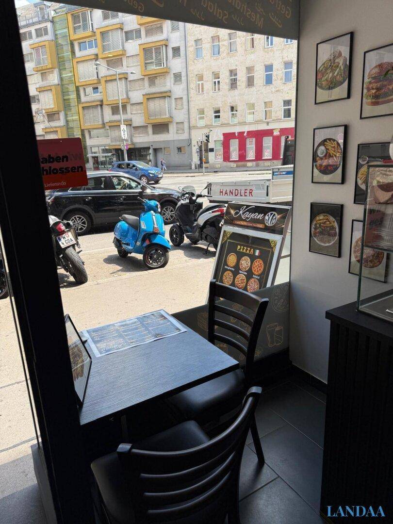 Sitzbereich mit Blick durch das große Fenster auf die belebte Straße und parkende Fahrzeuge.