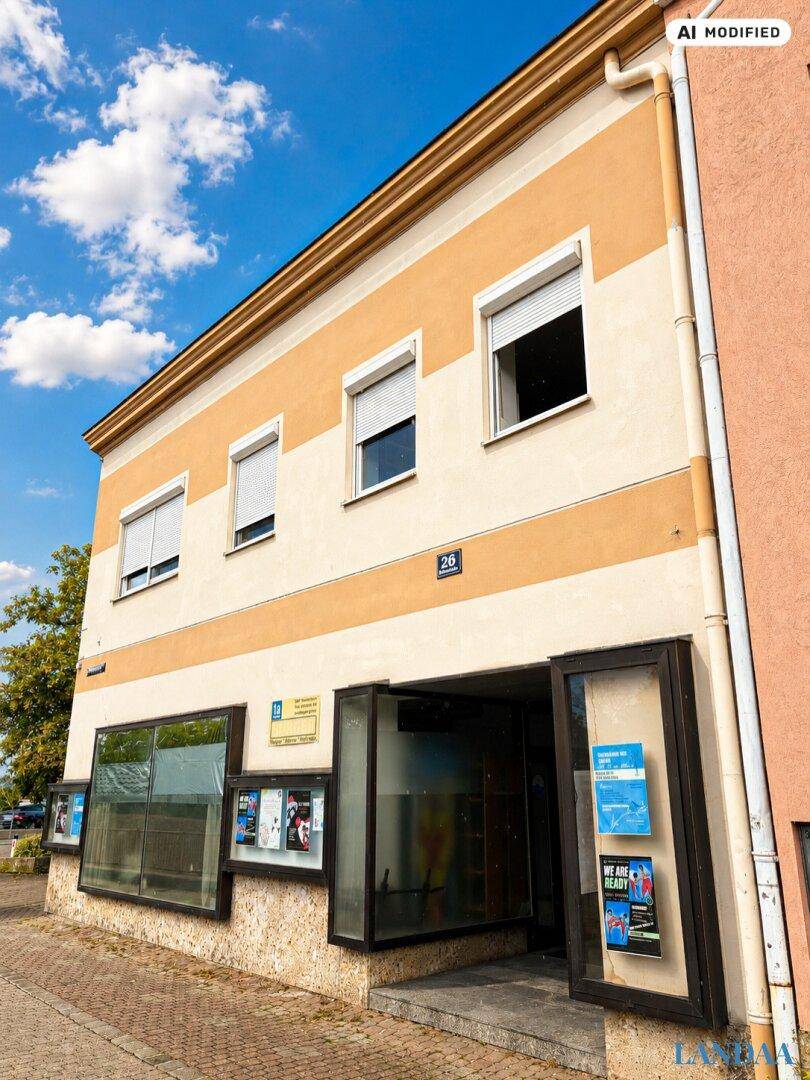Eingangsbereich eines Gebäudes mit gestreifter Fassade und großen Schaufenstern unter blauem Himmel.