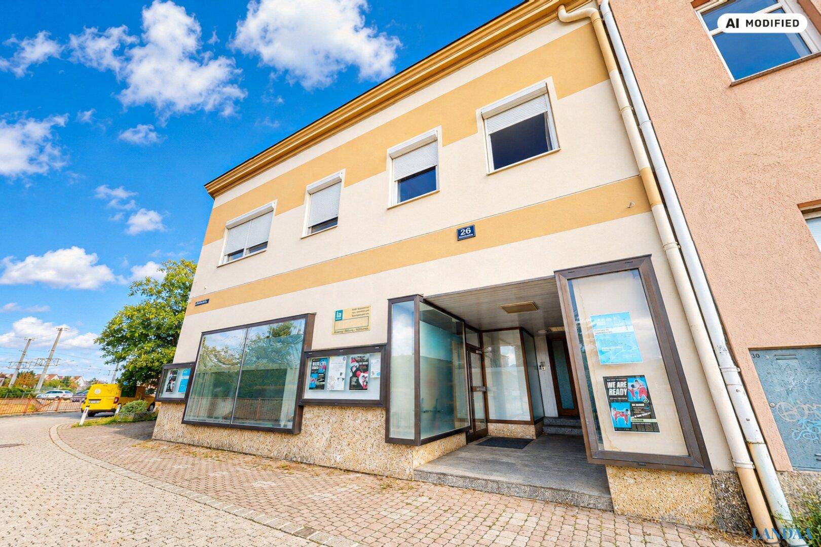 Eingangsbereich eines Gebäudes mit gestreifter Fassade und großen Schaufenstern unter blauem Himmel.