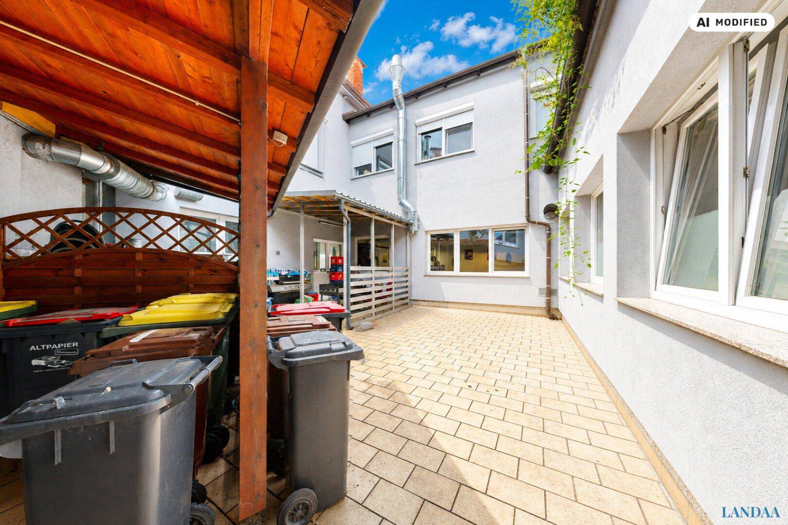 Gepflasterter Hinterhof mit Mülltonnen und überdachtem Bereich hinter dem Gebäude.