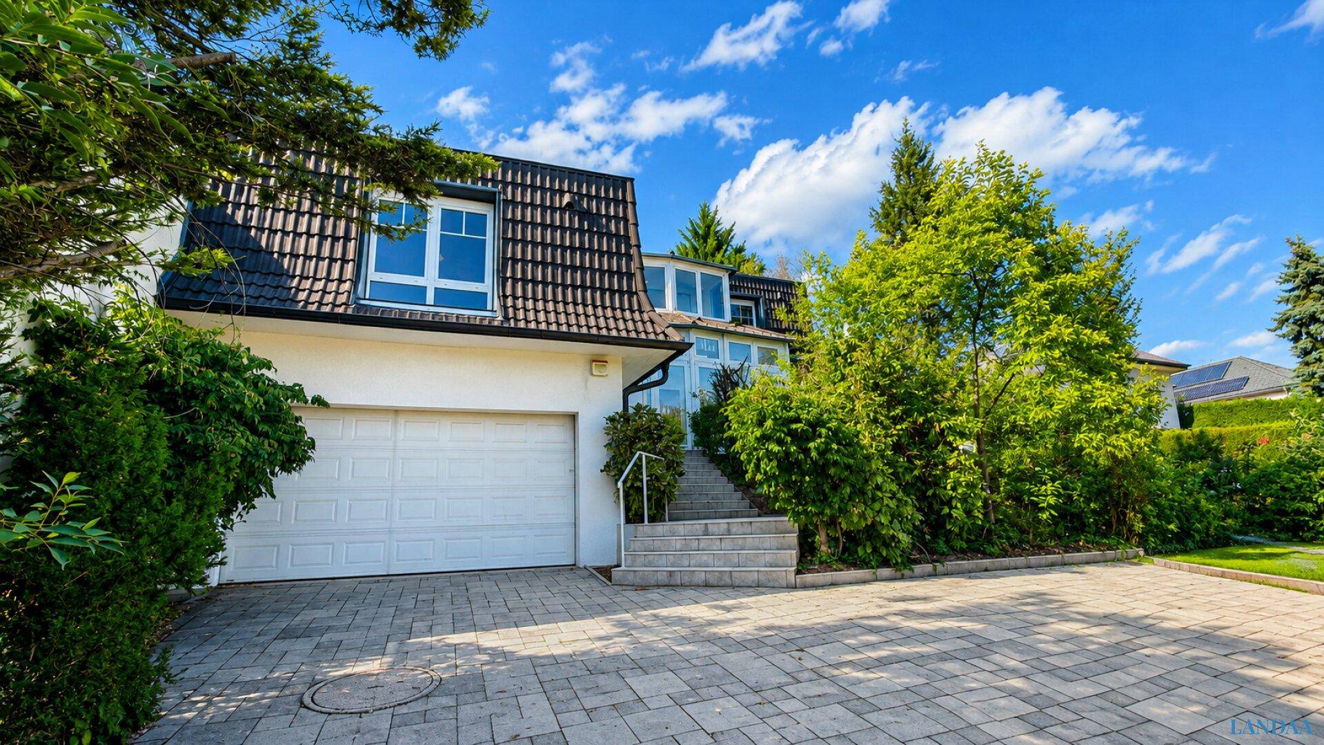 Vorderansicht des Hauses mit integrierter Garage, gepflasterter Auffahrt und Treppenzugang.