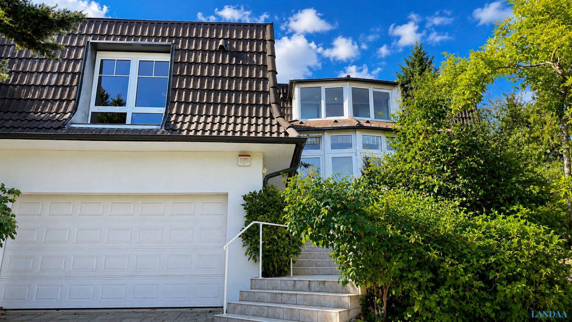 Ansicht des Hauses mit Garage und dem Eingangsbereich, umgeben von üppigem Grün.