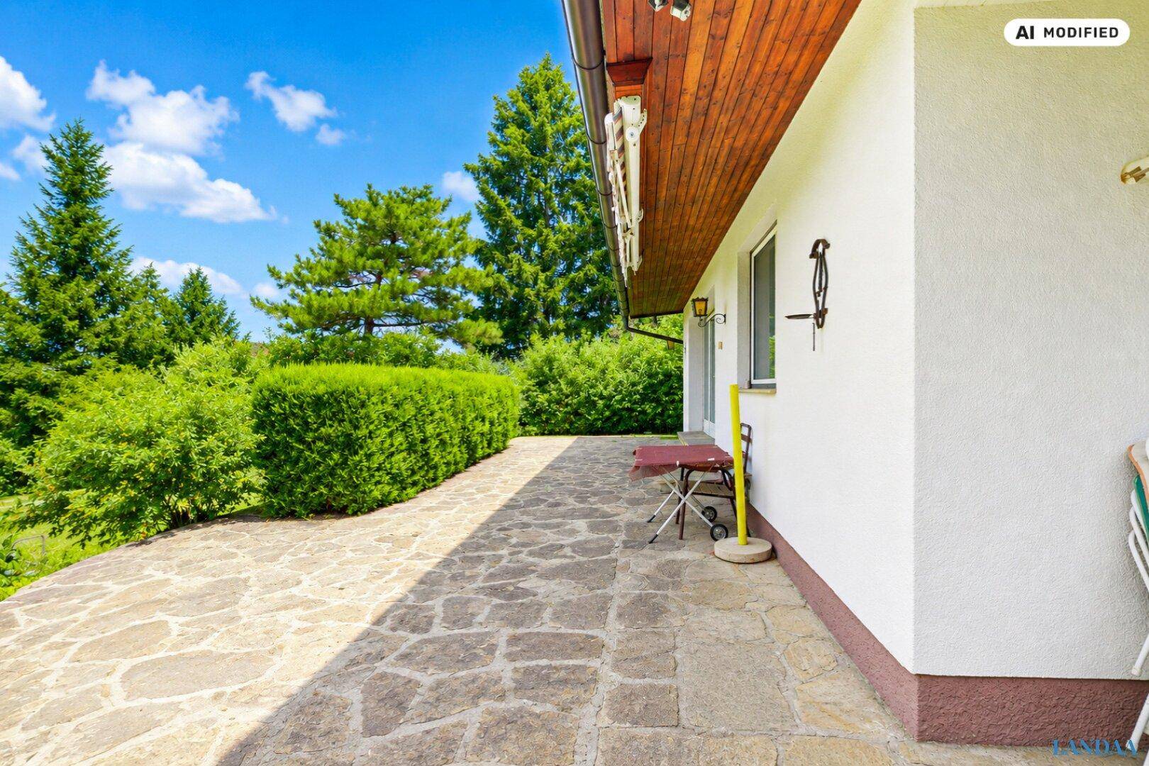 Seitliche Terrasse mit rustikalen Steinplatten und einfacher Bestuhlung, umgeben von viel Grün.