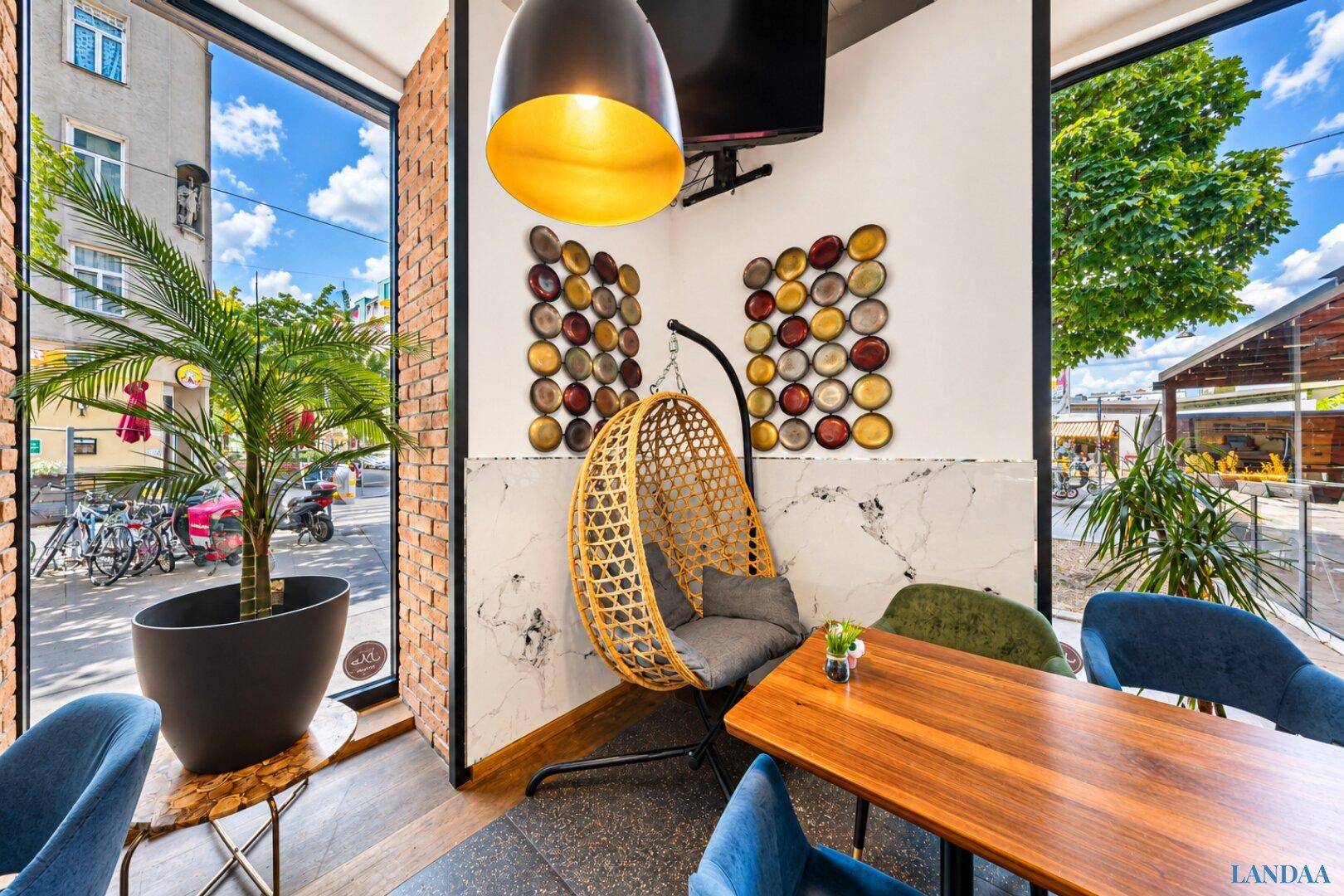 Gemütliche Ecke im Restaurant mit Hängesessel, großen Fenstern und Blick auf die Straße.