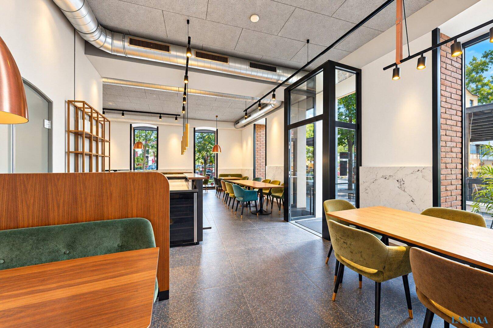 Langer Restaurantbereich mit verschiedenen Sitzgelegenheiten, hohen Decken und industriellen Lüftungsrohren.