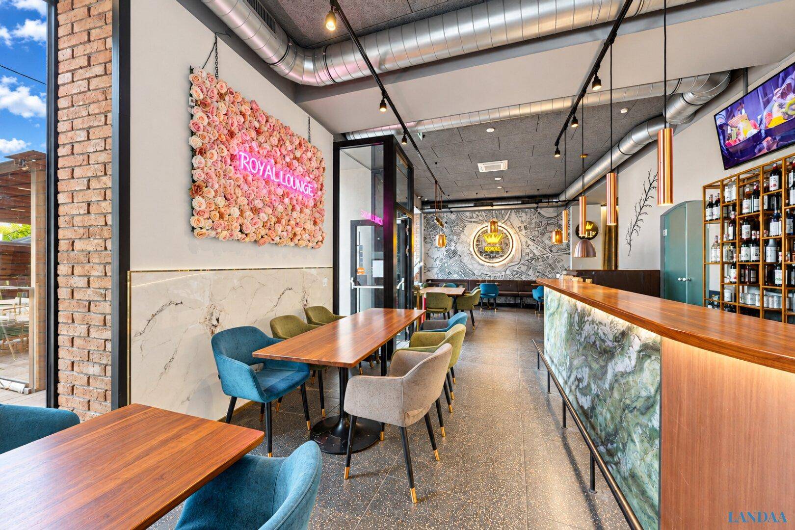 Moderner Restaurantbereich mit Bar, Neonlicht und floraler Wanddekoration, bietet vielfältige Sitzmöglichkeiten.
