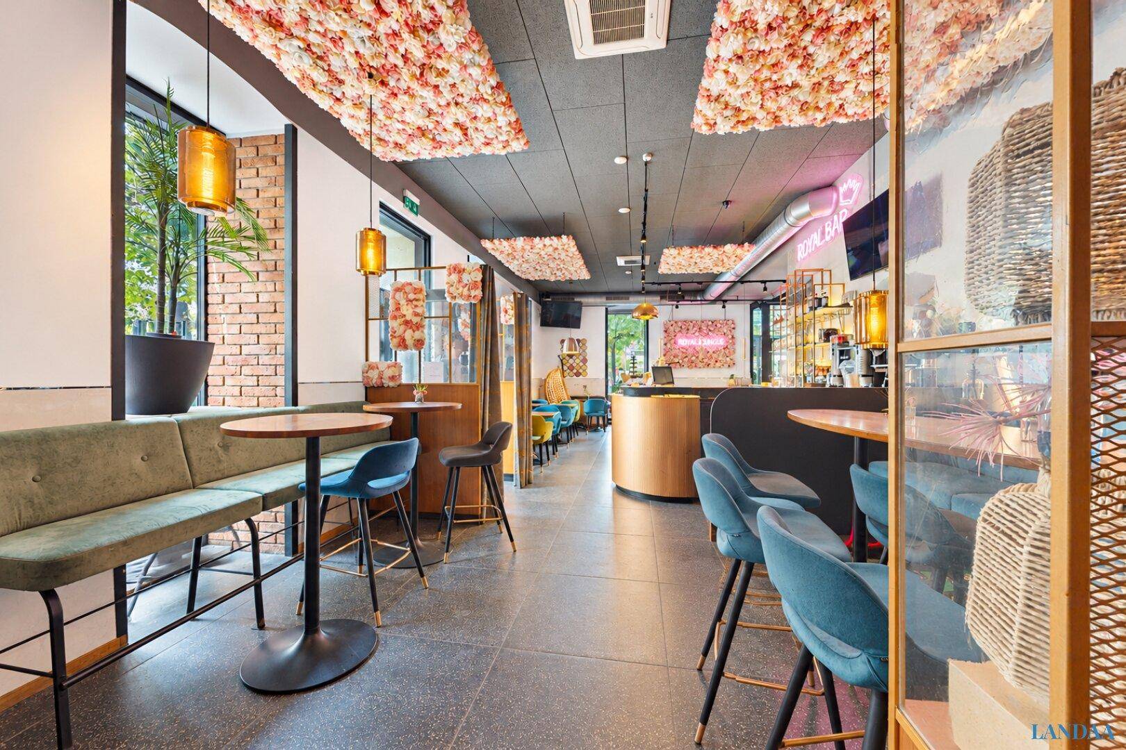 Heller Restaurantbereich mit Barhockern, Bänken und floralen Deckendekorationen, die eine einladende Atmosphäre schaffen.