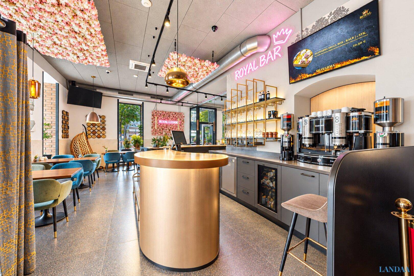 Elegante Bar im Restaurant mit Kaffeemaschinen, goldenem Tresen und floralen Deckendekorationen.
