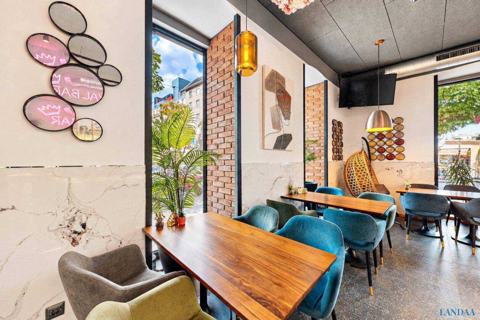 Gemütlicher Restaurantbereich mit Holztischen, blauen Stühlen und großen Fenstern mit Blick nach draußen.