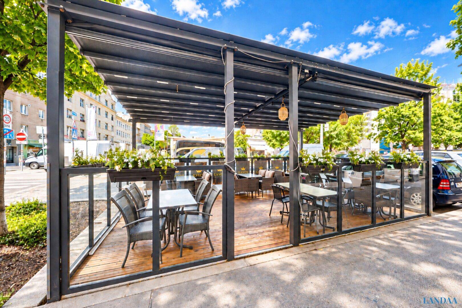 Überdachte Außenterrasse des Restaurants mit Tischen, Stühlen und Blumenkästen, ideal für Mahlzeiten im Freien.