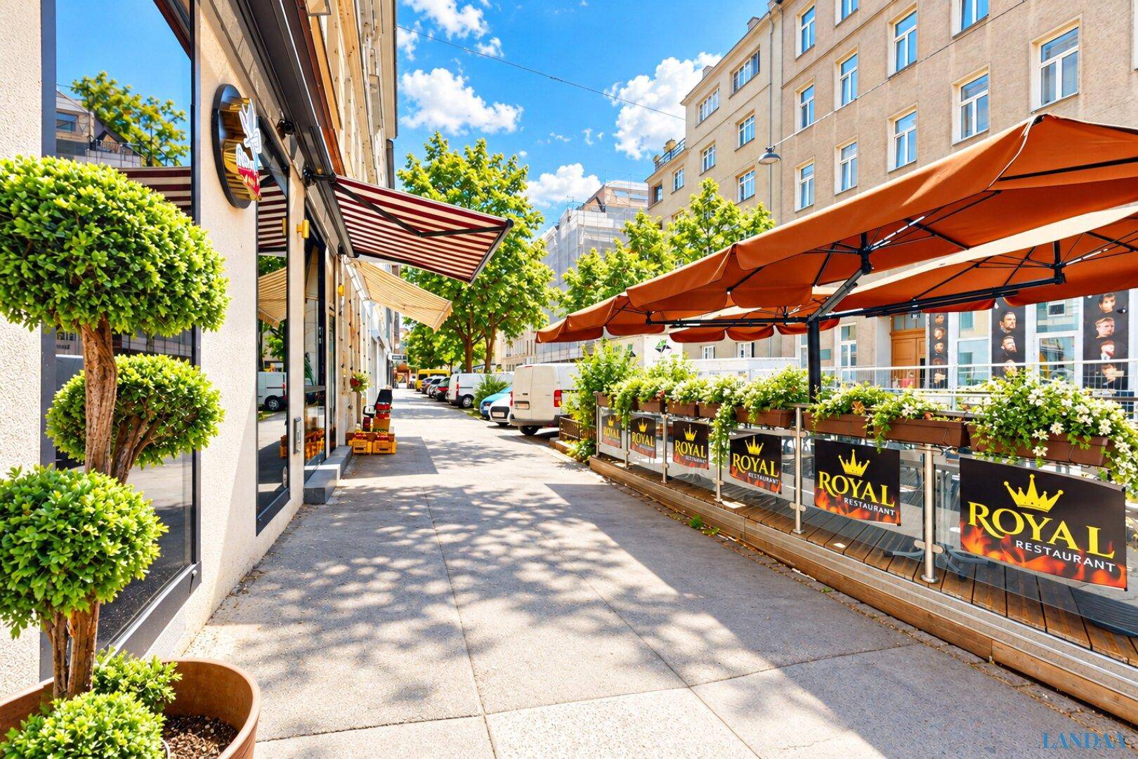 Gehweg vor dem Restaurant mit Sonnenschirmen, Blumenkästen und Blick auf die belebte Straße.