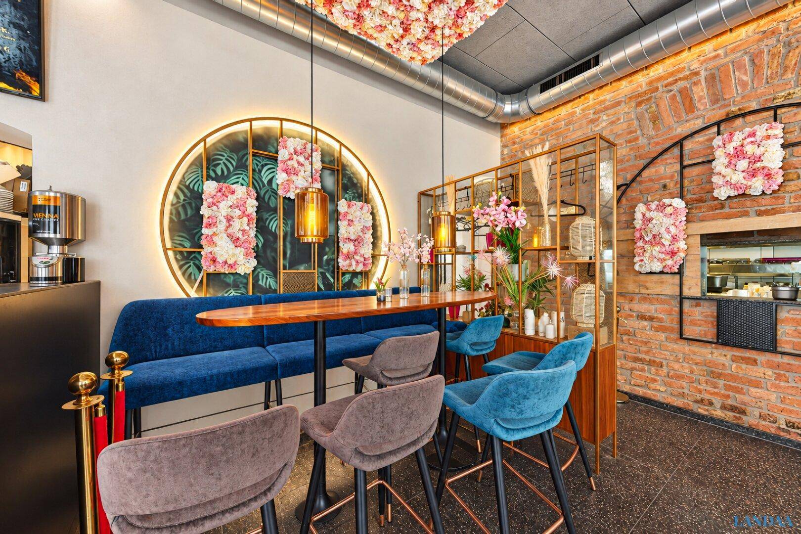 Stilvoller Restaurantbereich mit blauer Sitzbank, Holztisch und floralen Dekorationen an der Decke und Wand.
